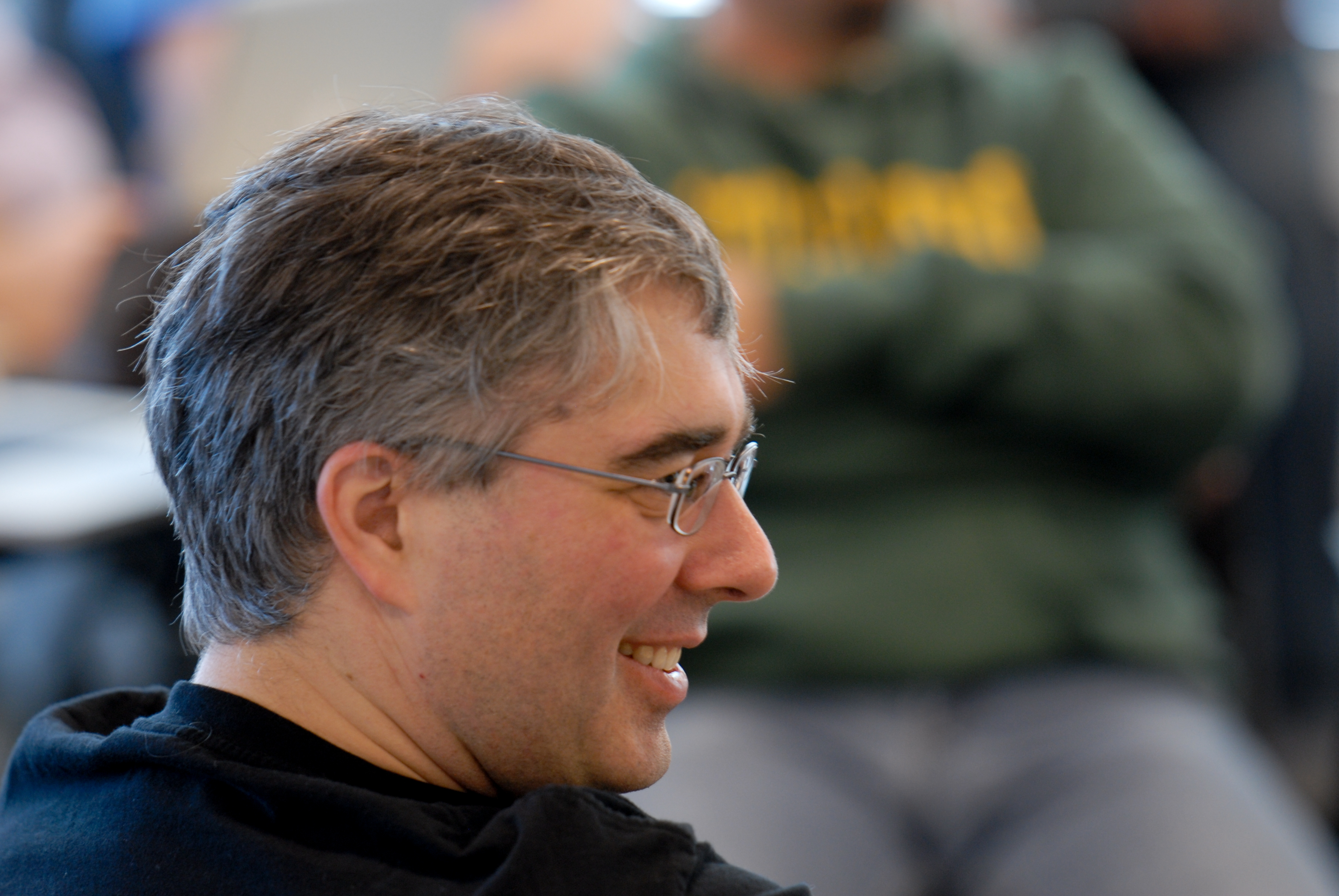 A man with glasses and gray hair smiles while attending an event or meeting.