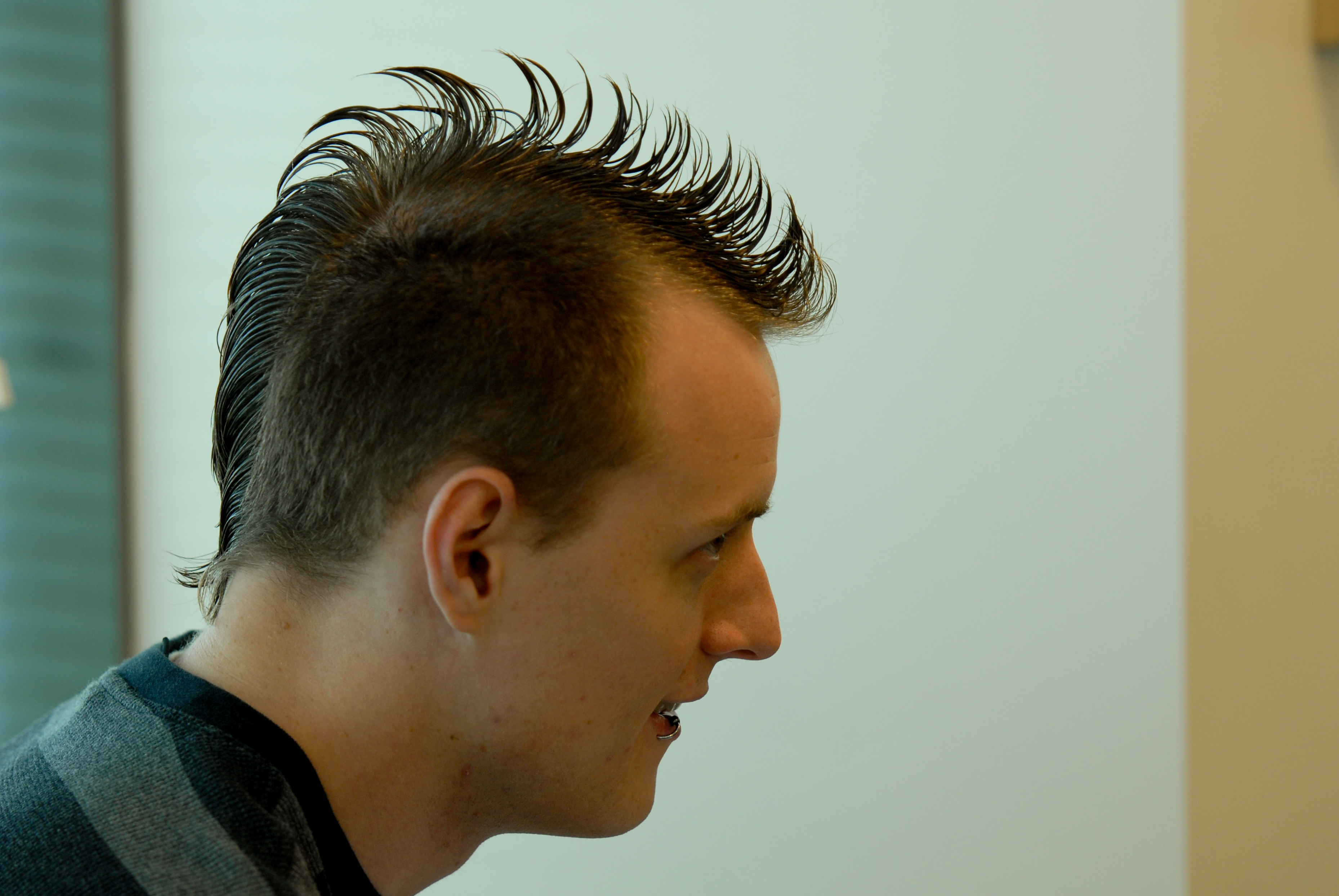 A person with a spiky mohawk hairstyle is looking to the side in an indoor setting.