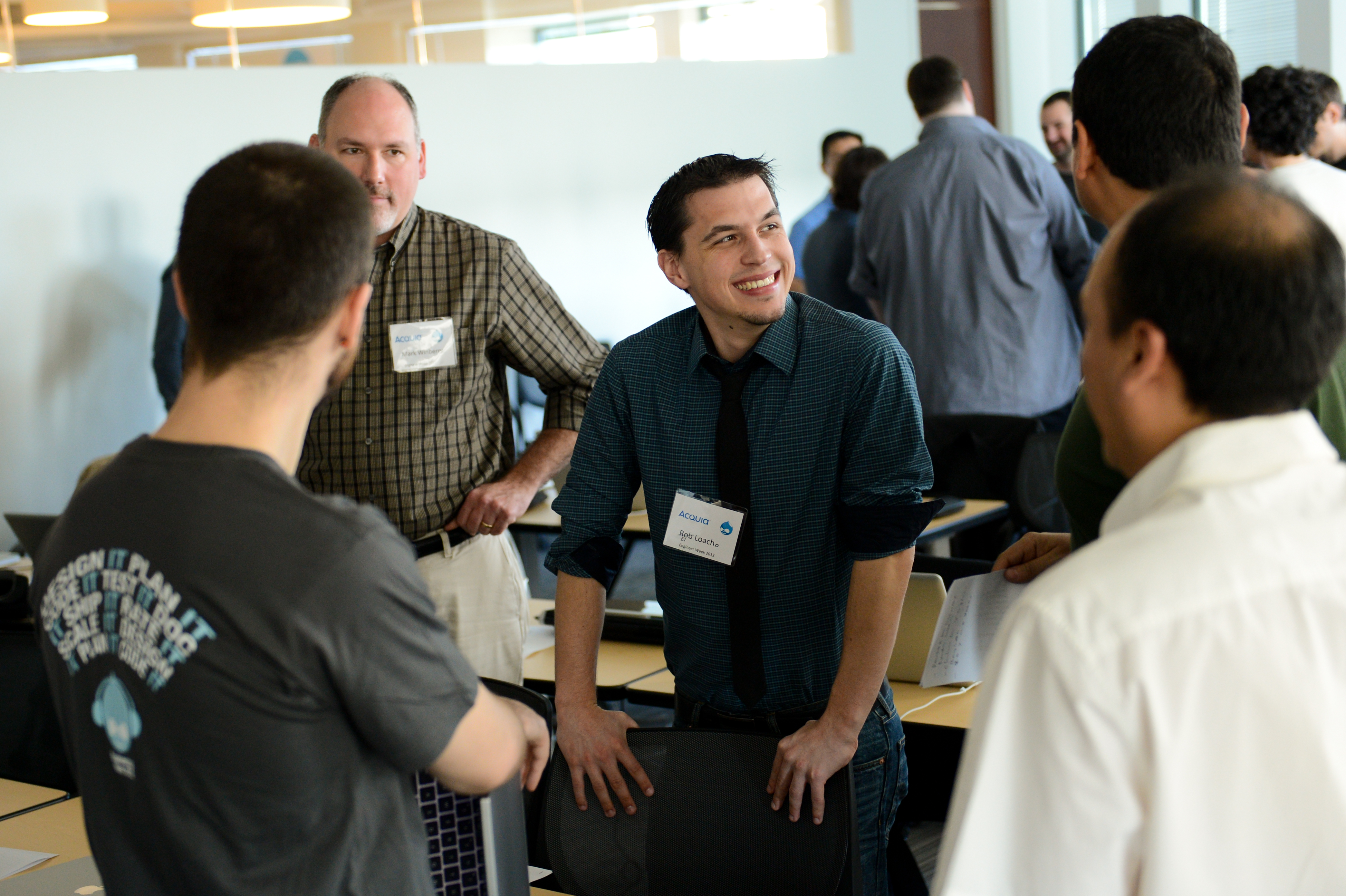 A group of people engaged in conversation at a professional event, with one person smiling and leaning on a chair.