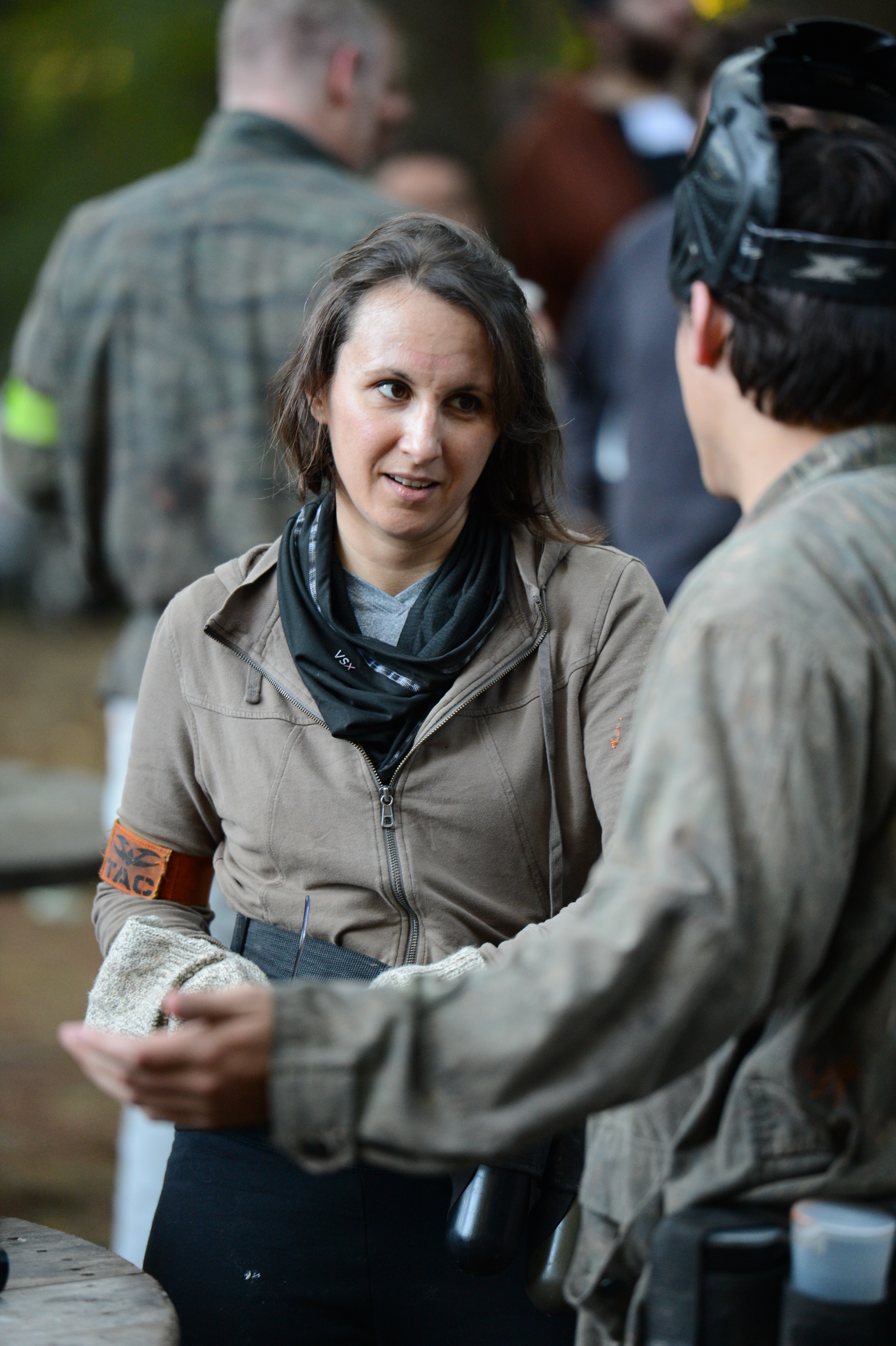 Two people in paintball gear are having a conversation, with one gesturing while the other listens attentively.