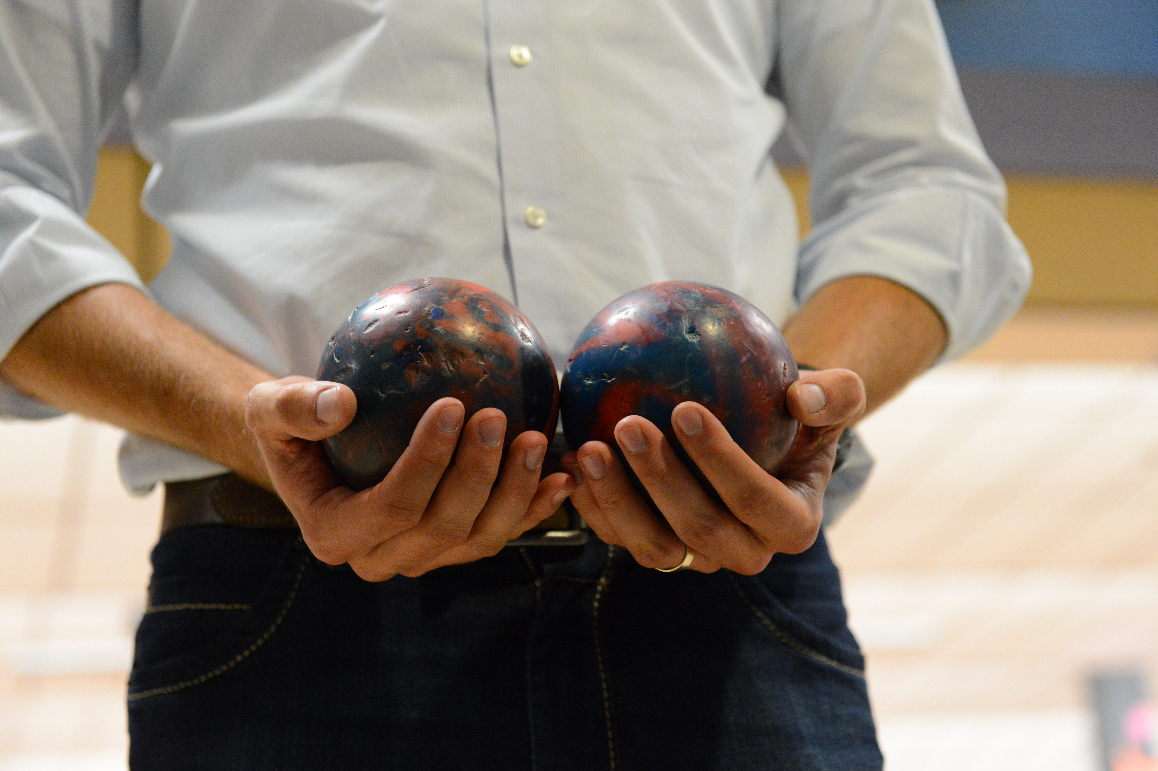 A person in a light-colored shirt holds two small bowling balls, one in each hand.