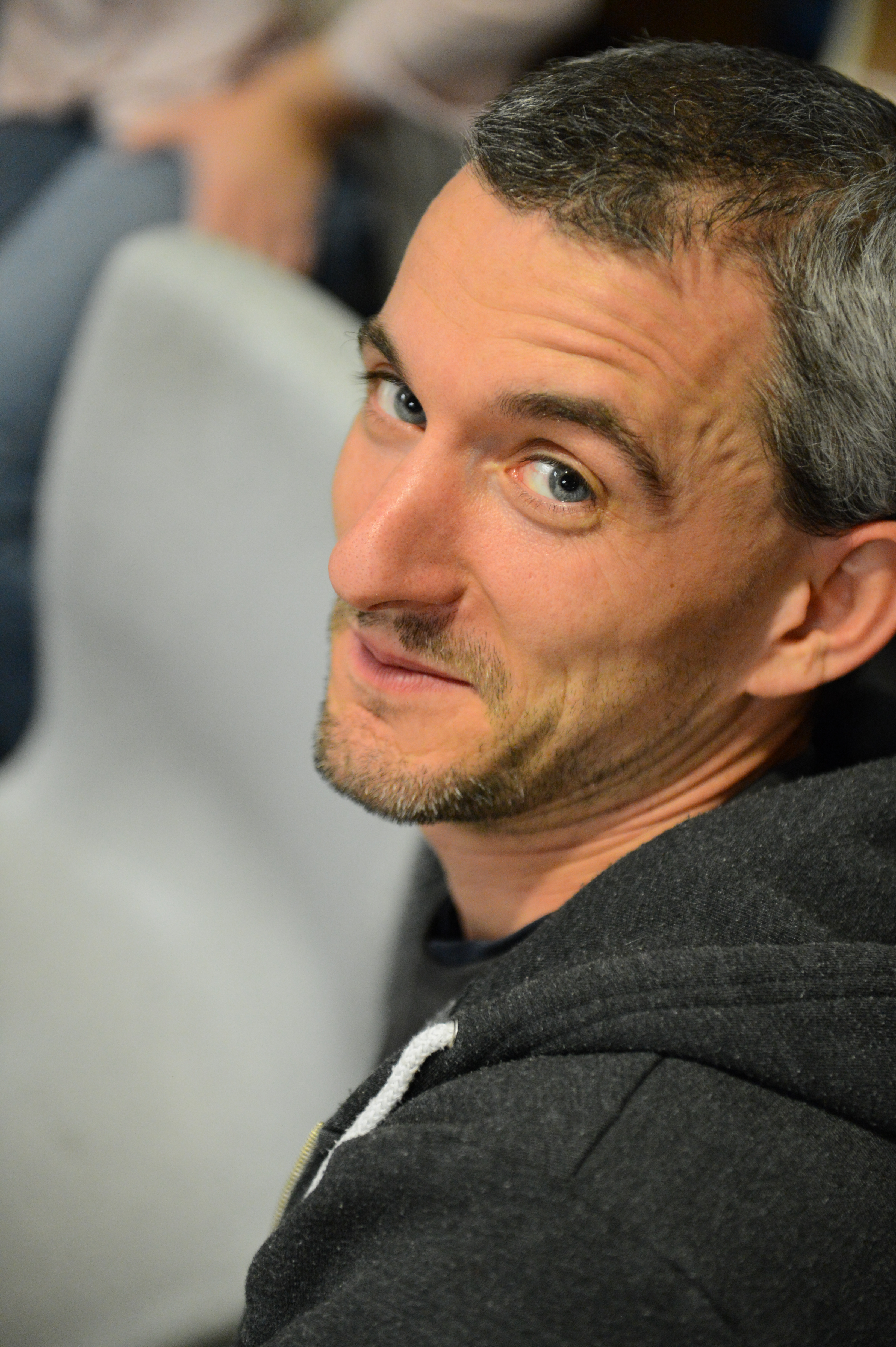 A man in a dark hoodie looks back at the camera with a slight smile.