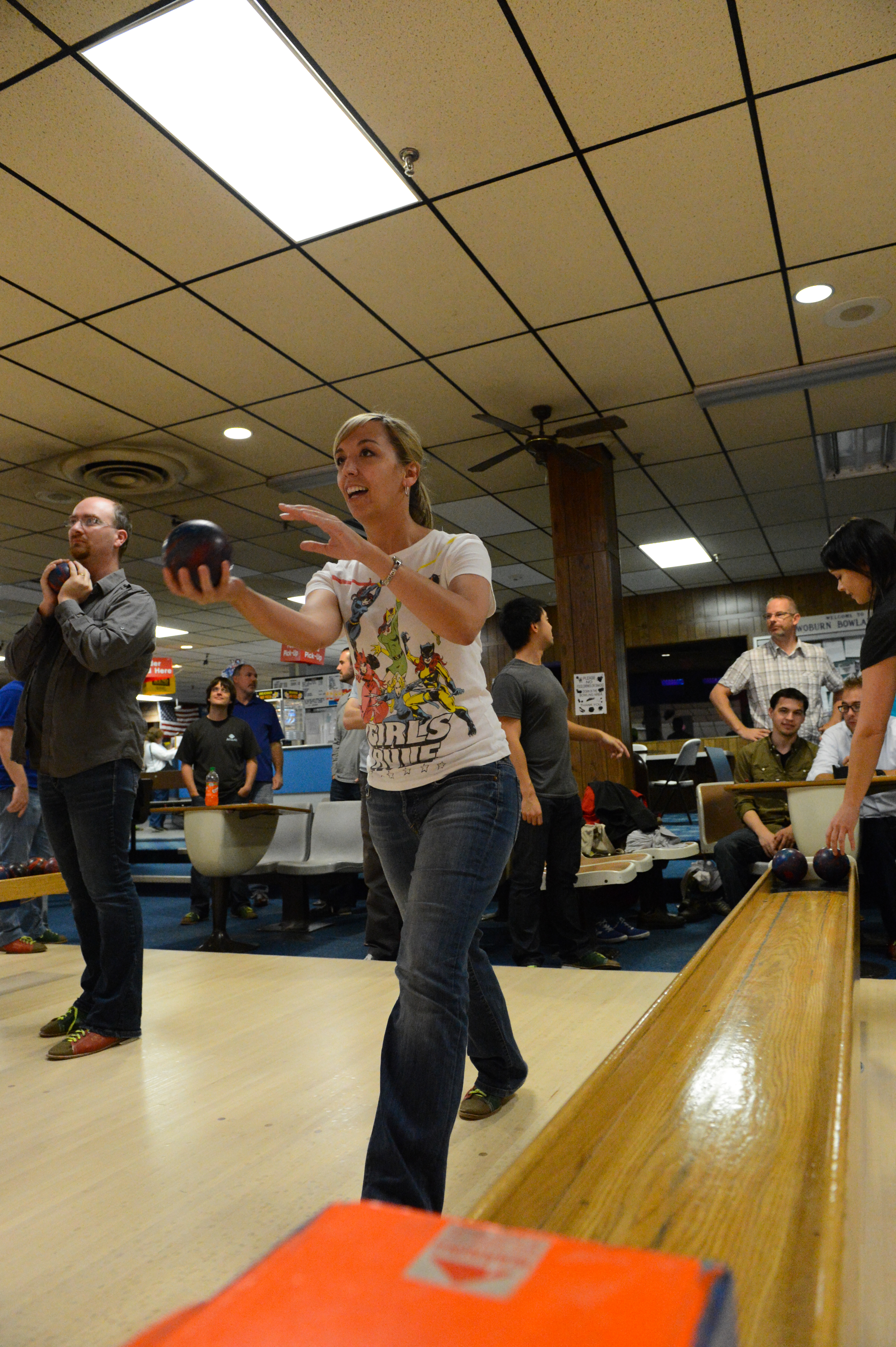 A woman prepares to throw a bowling ball while others watch and wait for their turn at the bowling alley.