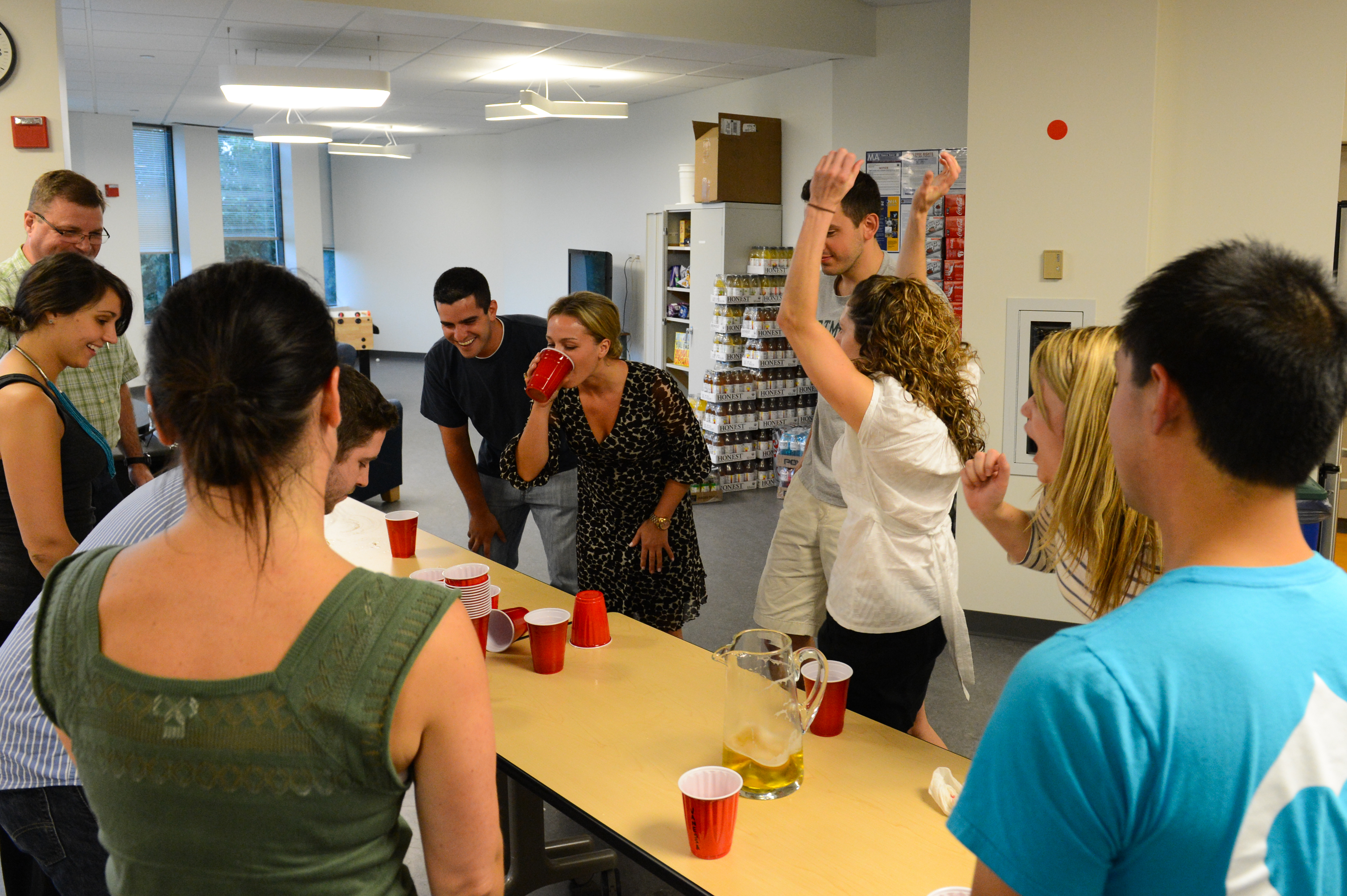 A group of people gathered around a table playing a drinking game, cheering and reacting with excitement.