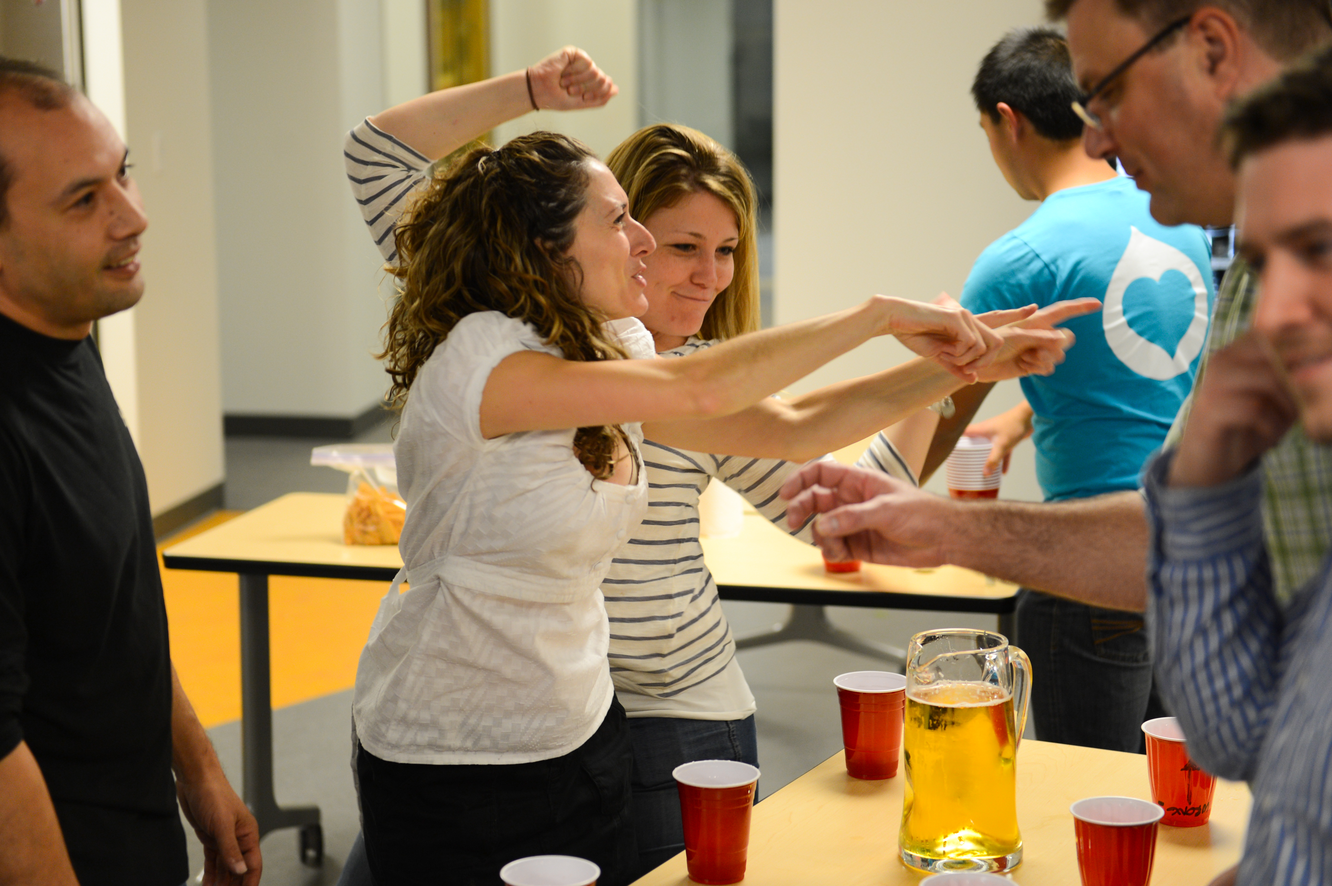 People at a party laughing and gesturing while playing a game with drinks on a table.