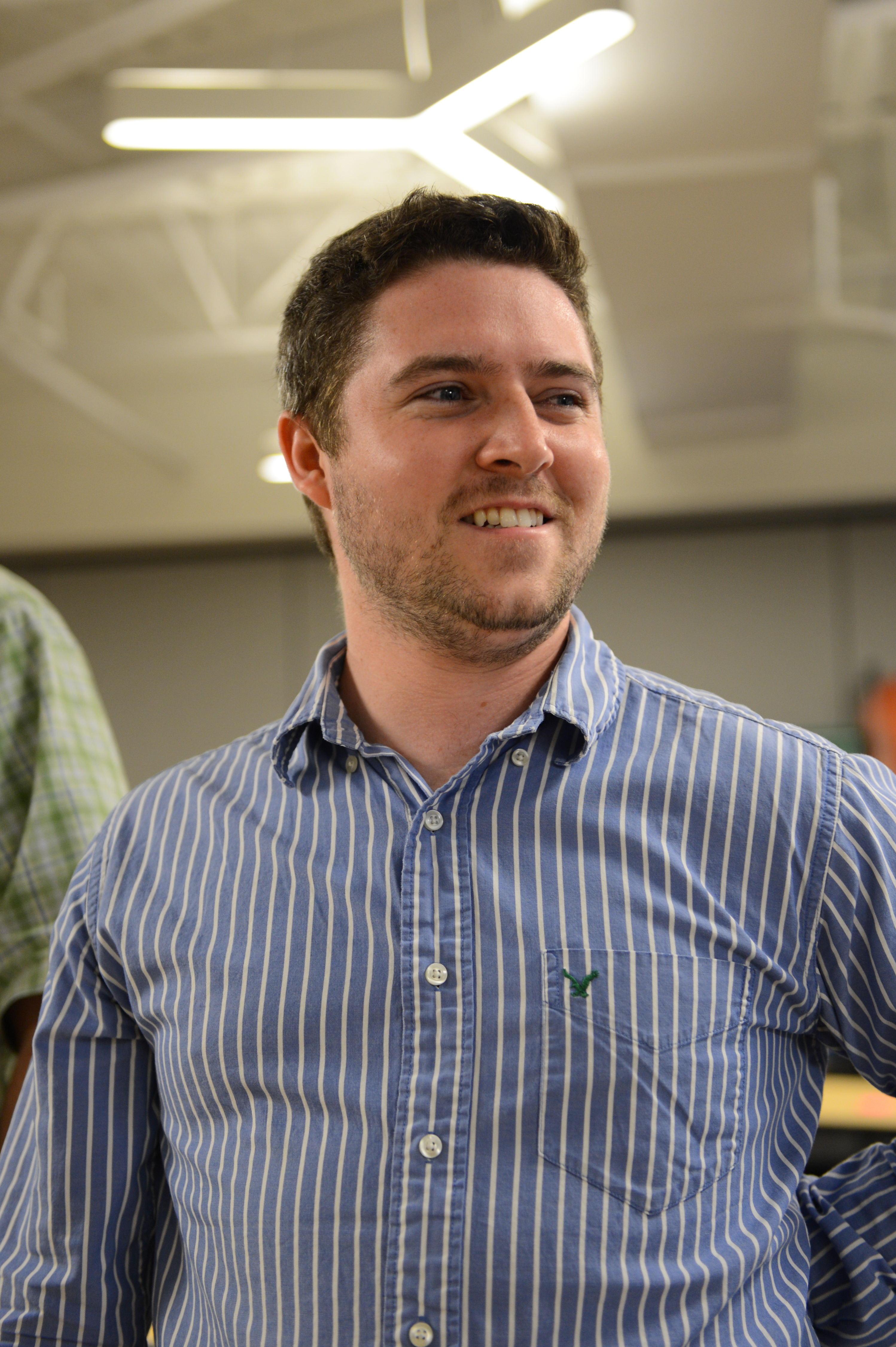 A man in a striped shirt smiles and looks to the side at a party.
