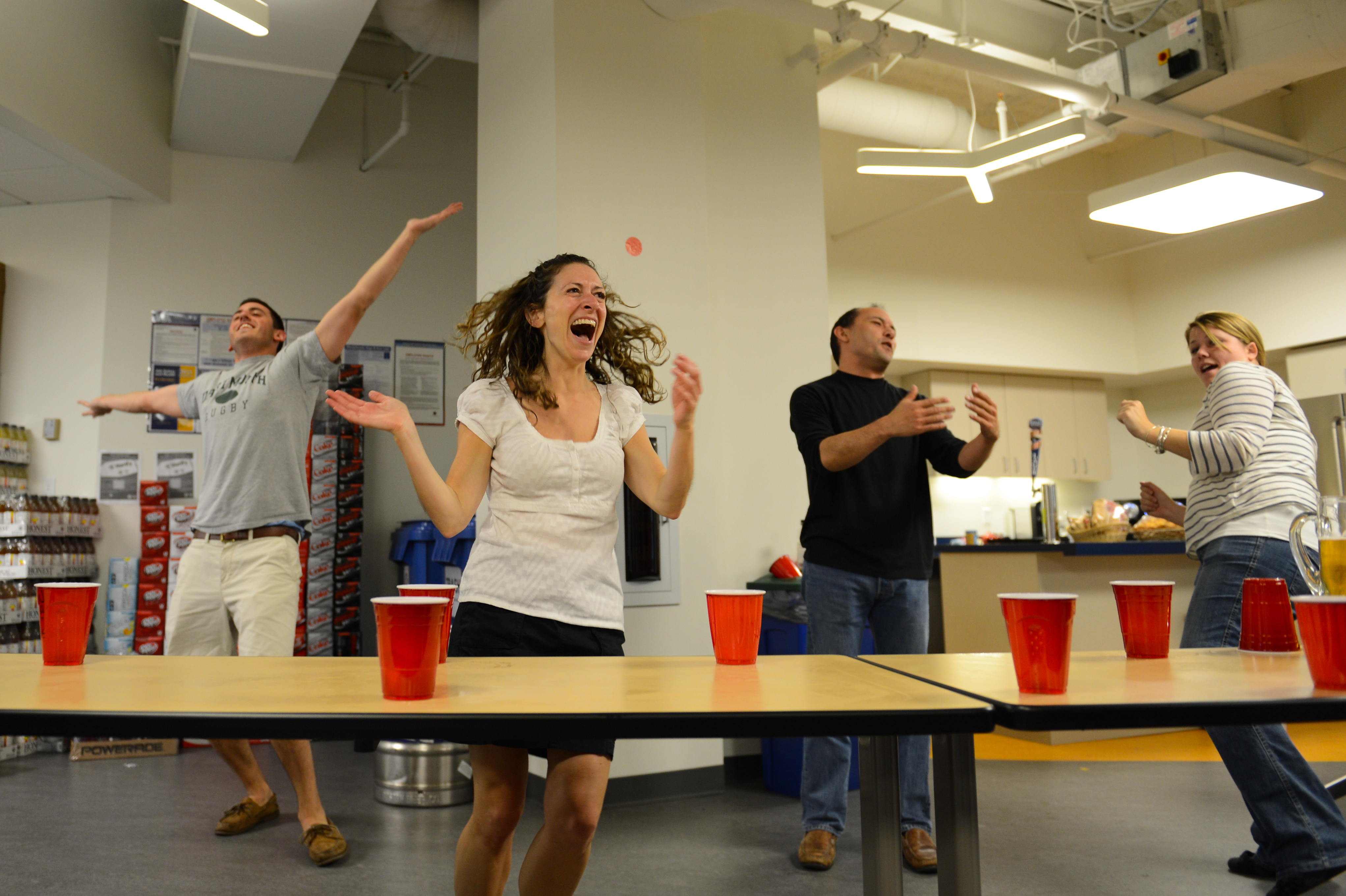 People are playing a party game with red cups, reacting with excitement and laughter in an indoor setting.