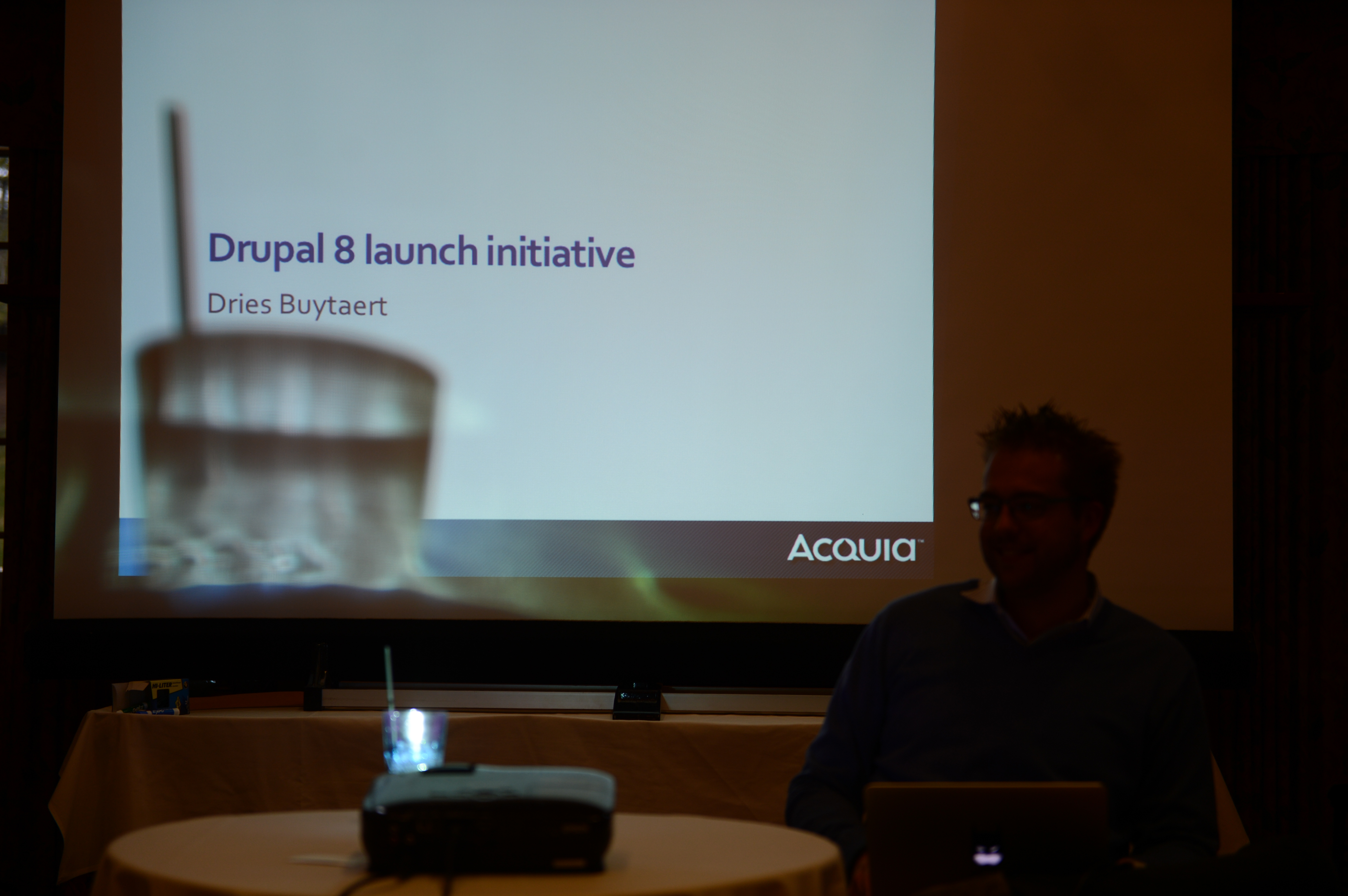 A presentation slide titled "Drupal 8 launch initiative" is displayed, with a speaker sitting in front of it.