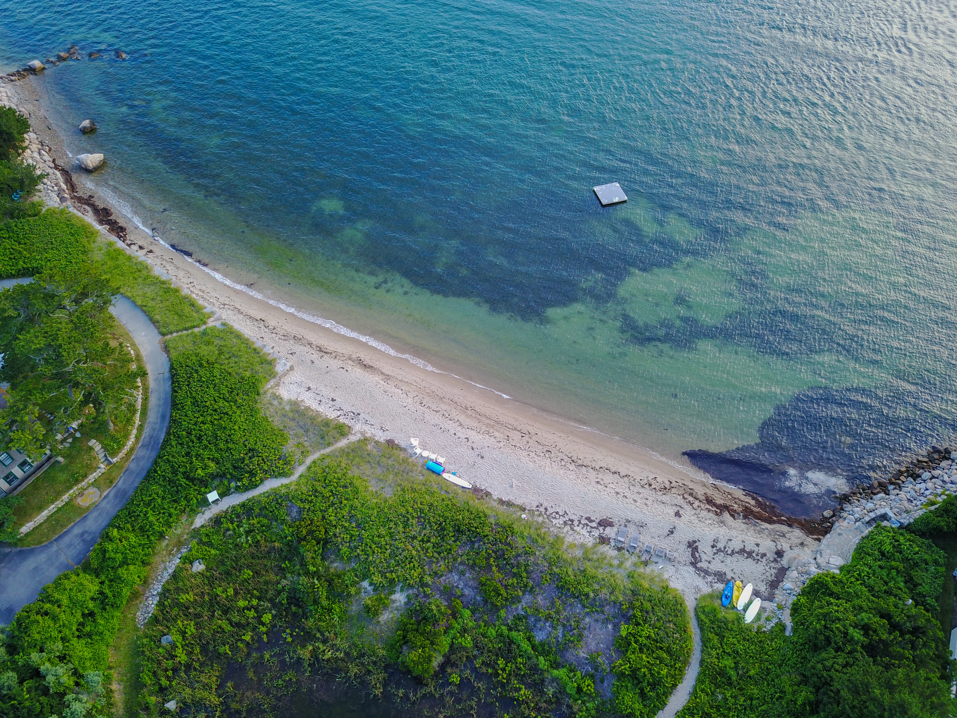 Aerial view of a sandy beach with small boats onshore and a floating platform in the clear water.