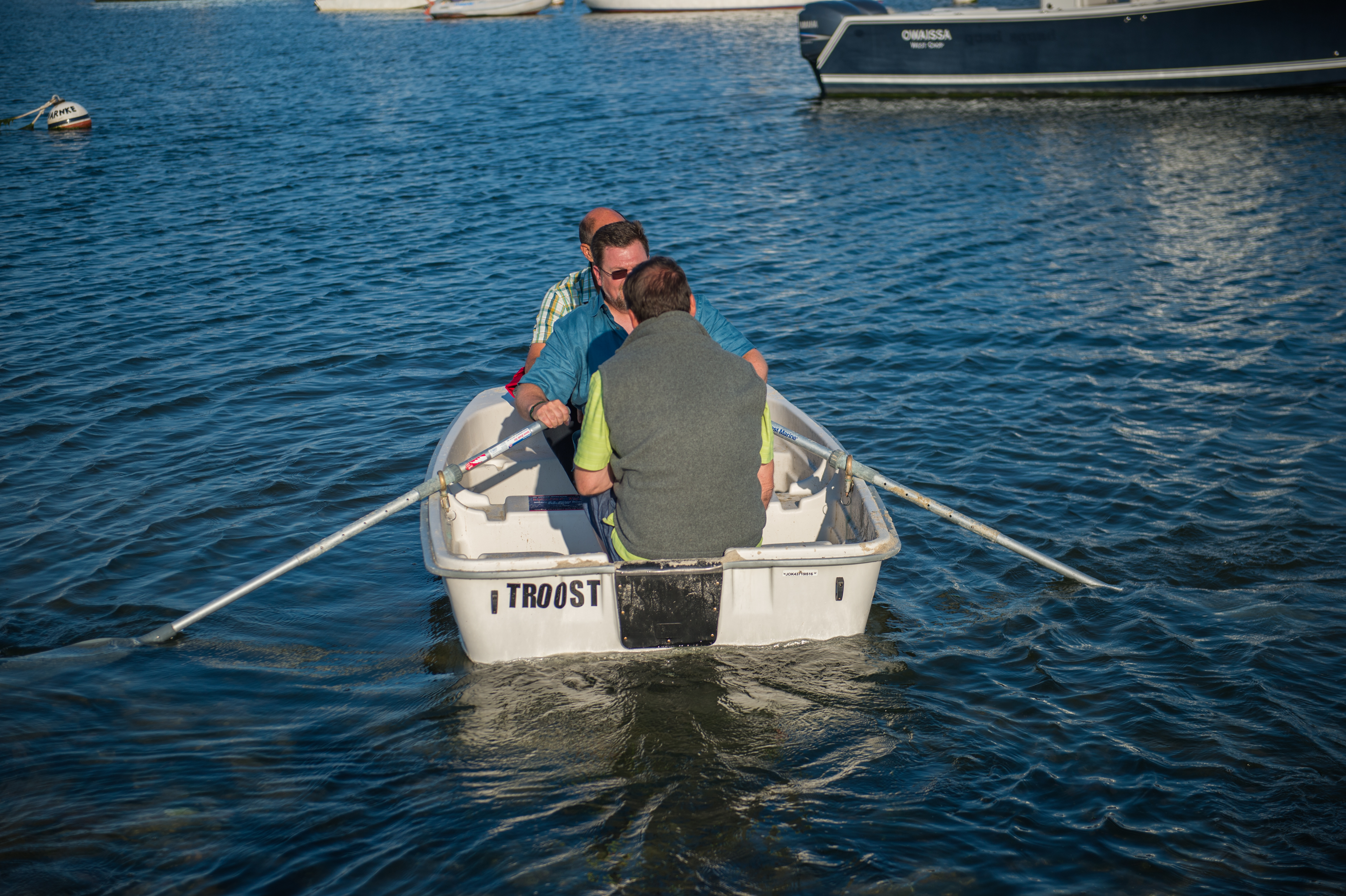 Two people rowing a small white boat on the water, with other boats visible in the background.