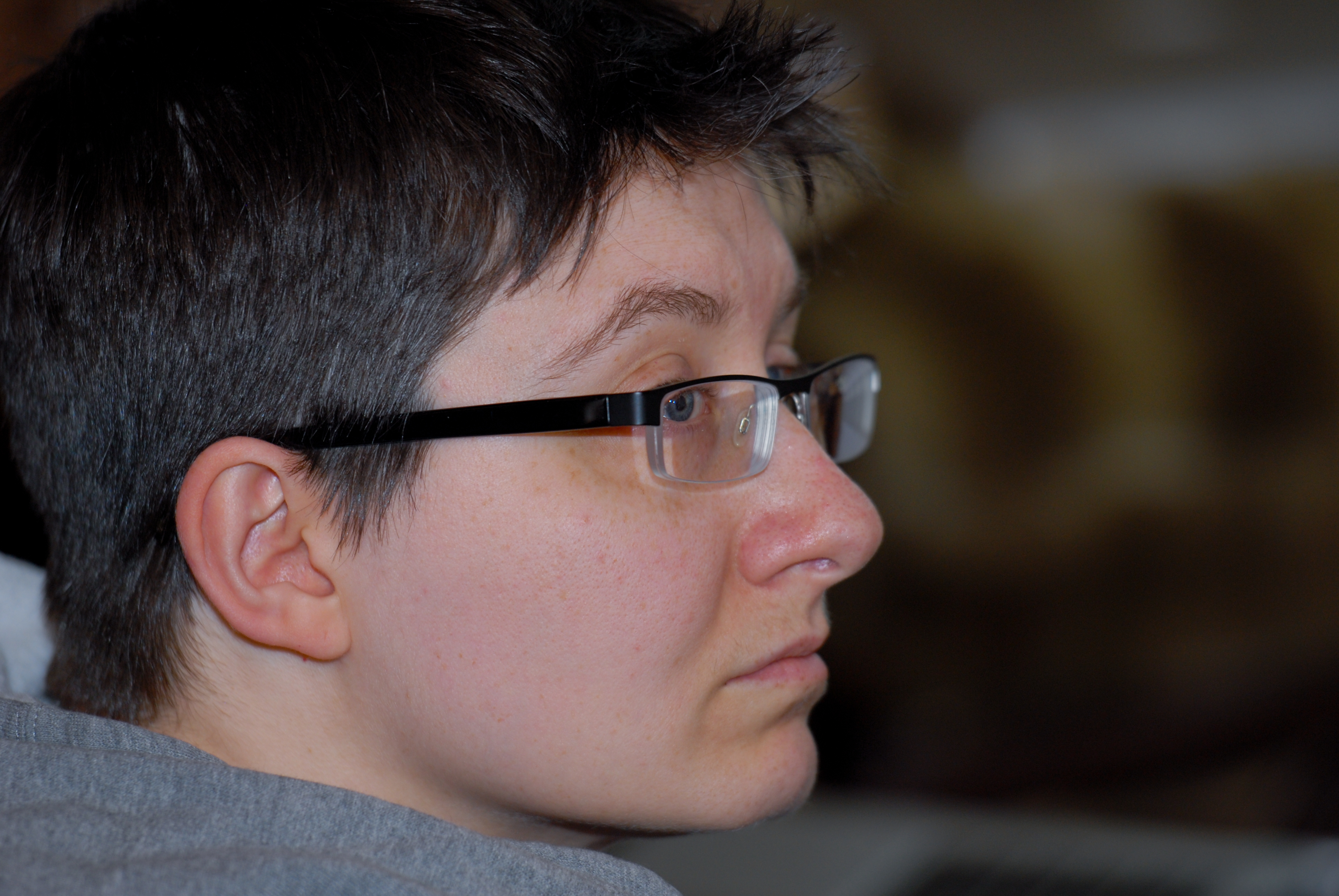 A person wearing glasses and a gray shirt looks attentively to the side in an indoor setting.