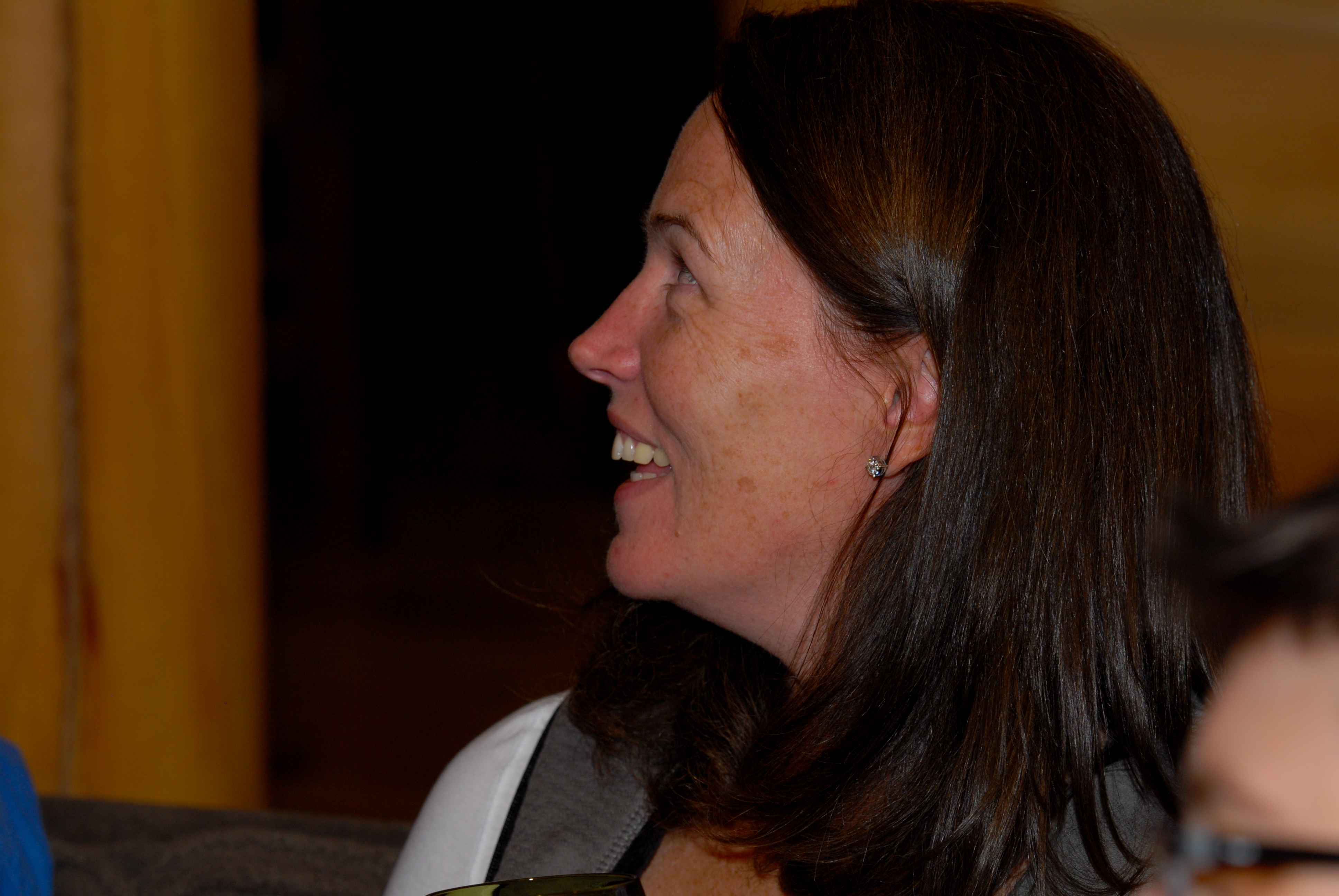 A woman with long brown hair smiles and looks to the side during an indoor event.