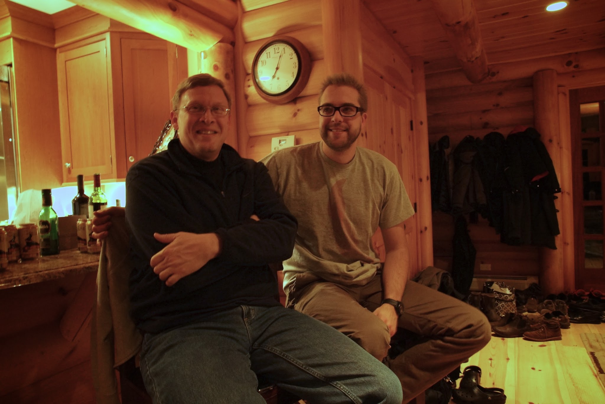 Two men sitting in a wooden cabin, smiling at the camera.