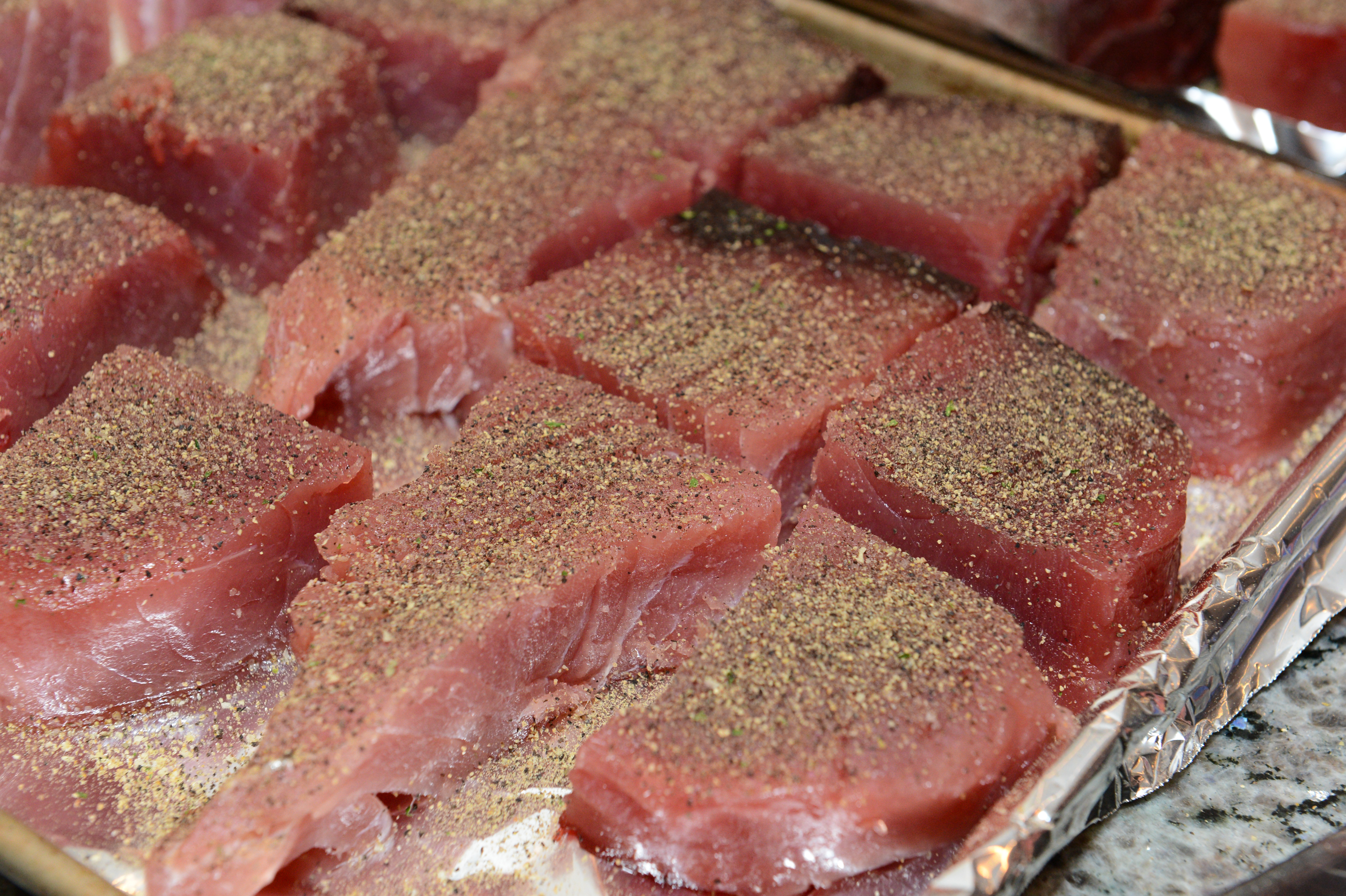 Raw tuna steaks coated with seasoning are arranged on a foil-lined baking sheet, ready for cooking.