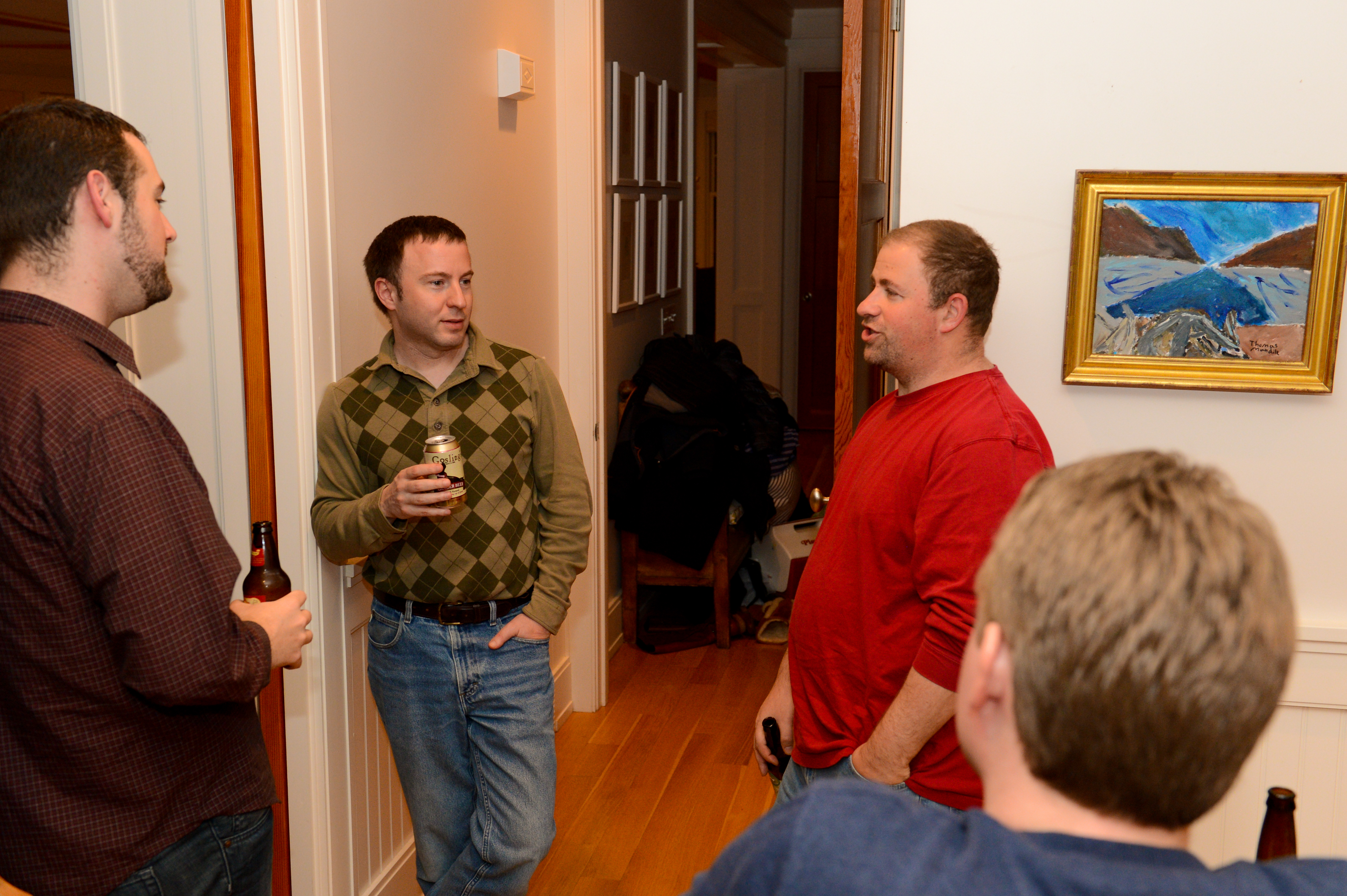 Four people stand in a hallway, holding drinks and engaged in conversation.