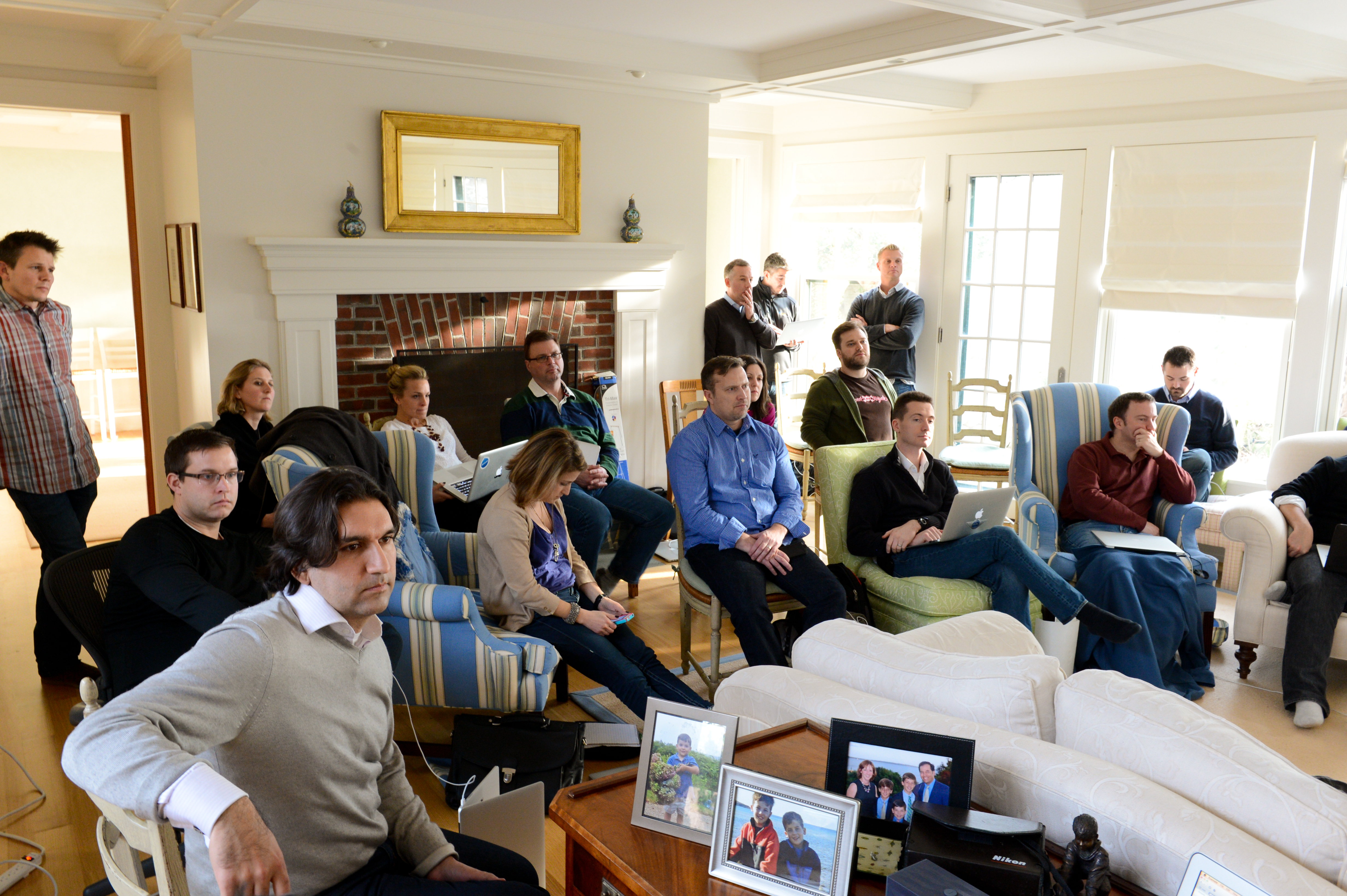 A group of people sits in a living room, attentively listening to a presentation or discussion.