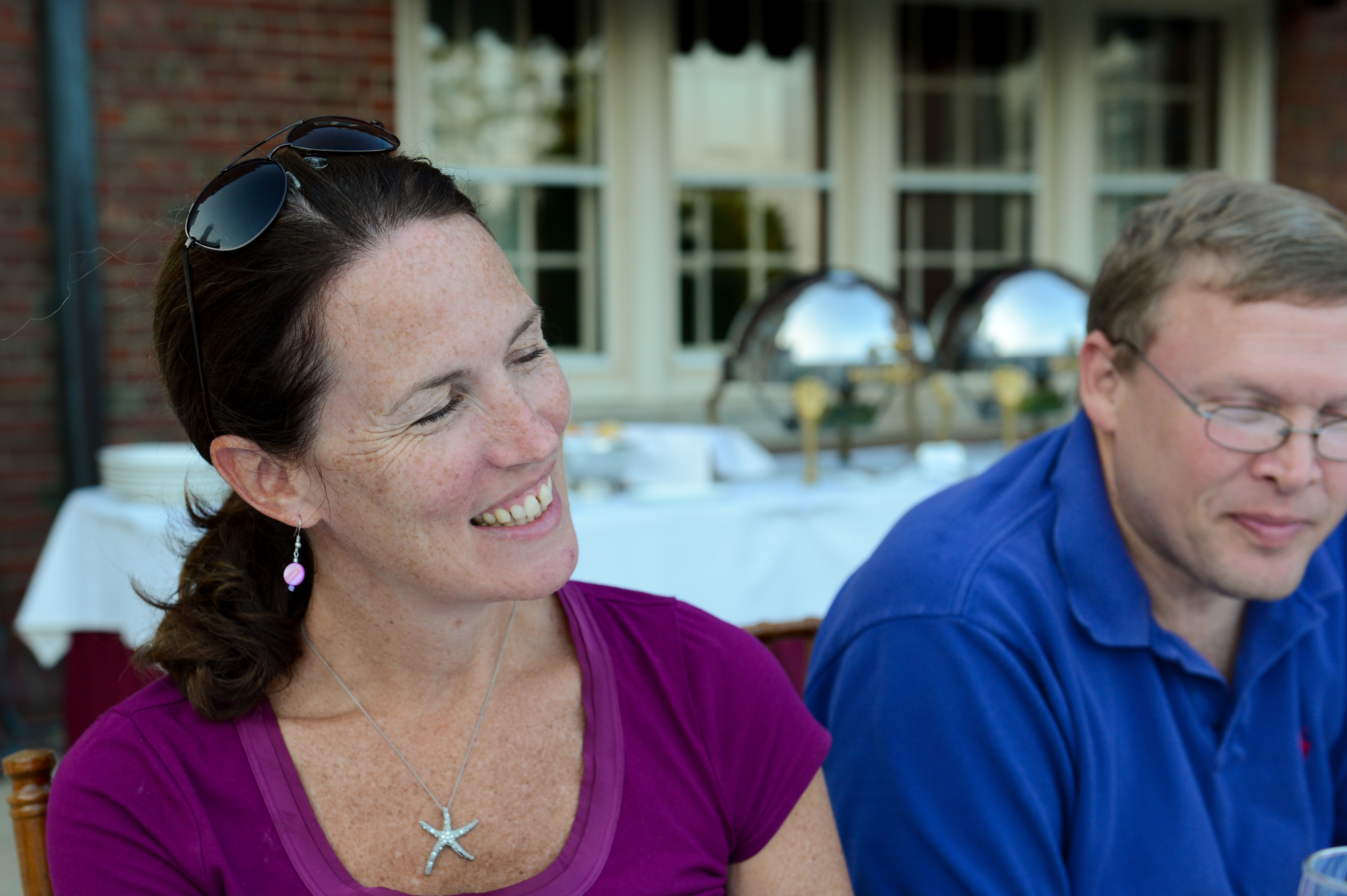 A woman in a purple shirt smiles while sitting next to a man in a blue shirt at dinner.