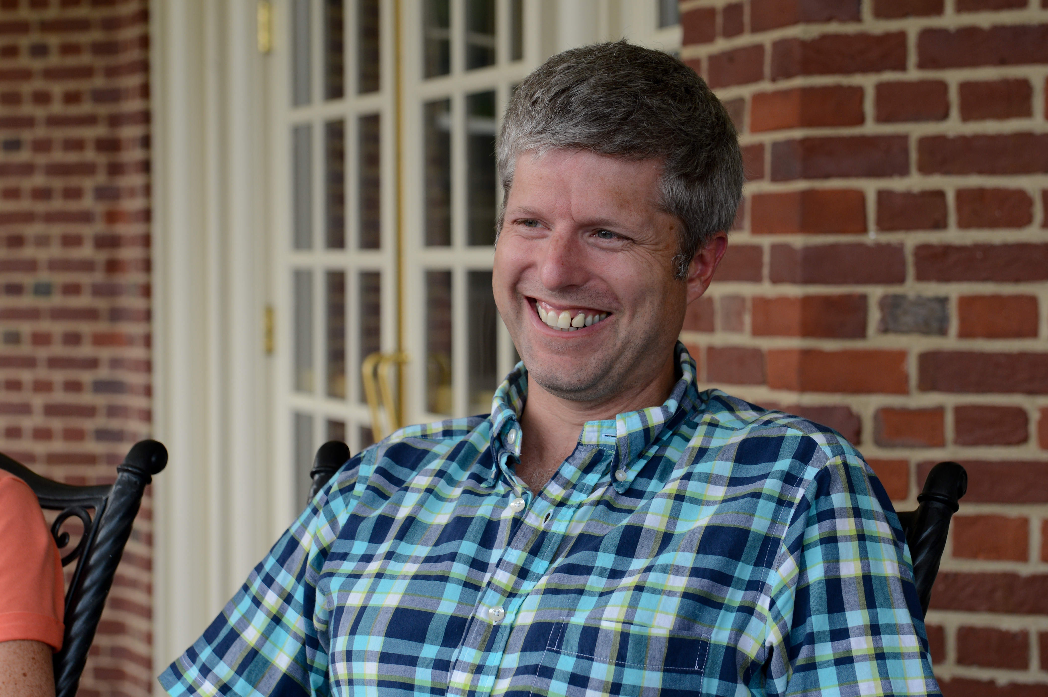 A man in a plaid shirt sits outside, smiling and engaged in conversation.