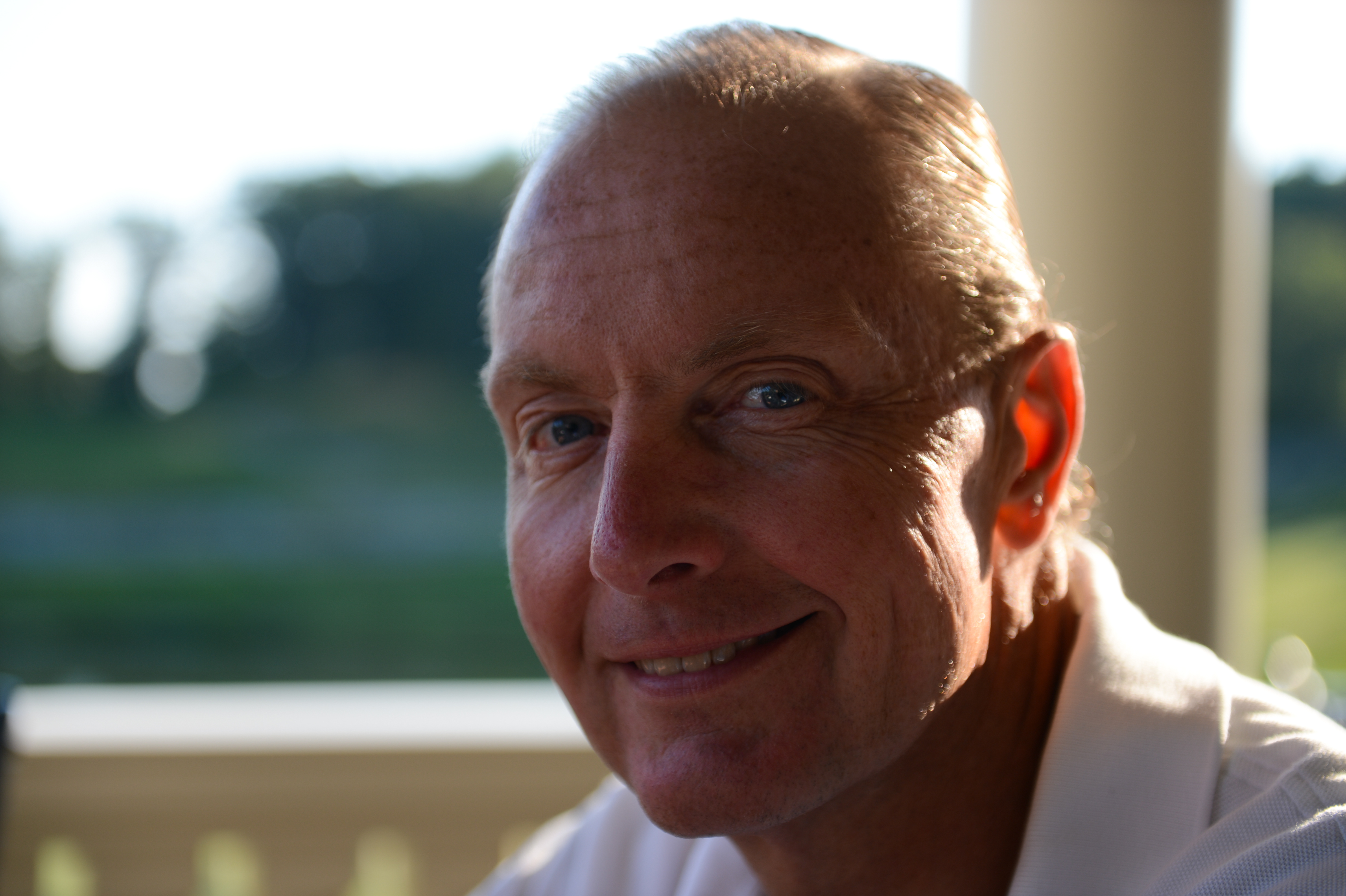 A man in a white shirt smiles while sitting outdoors in natural light.