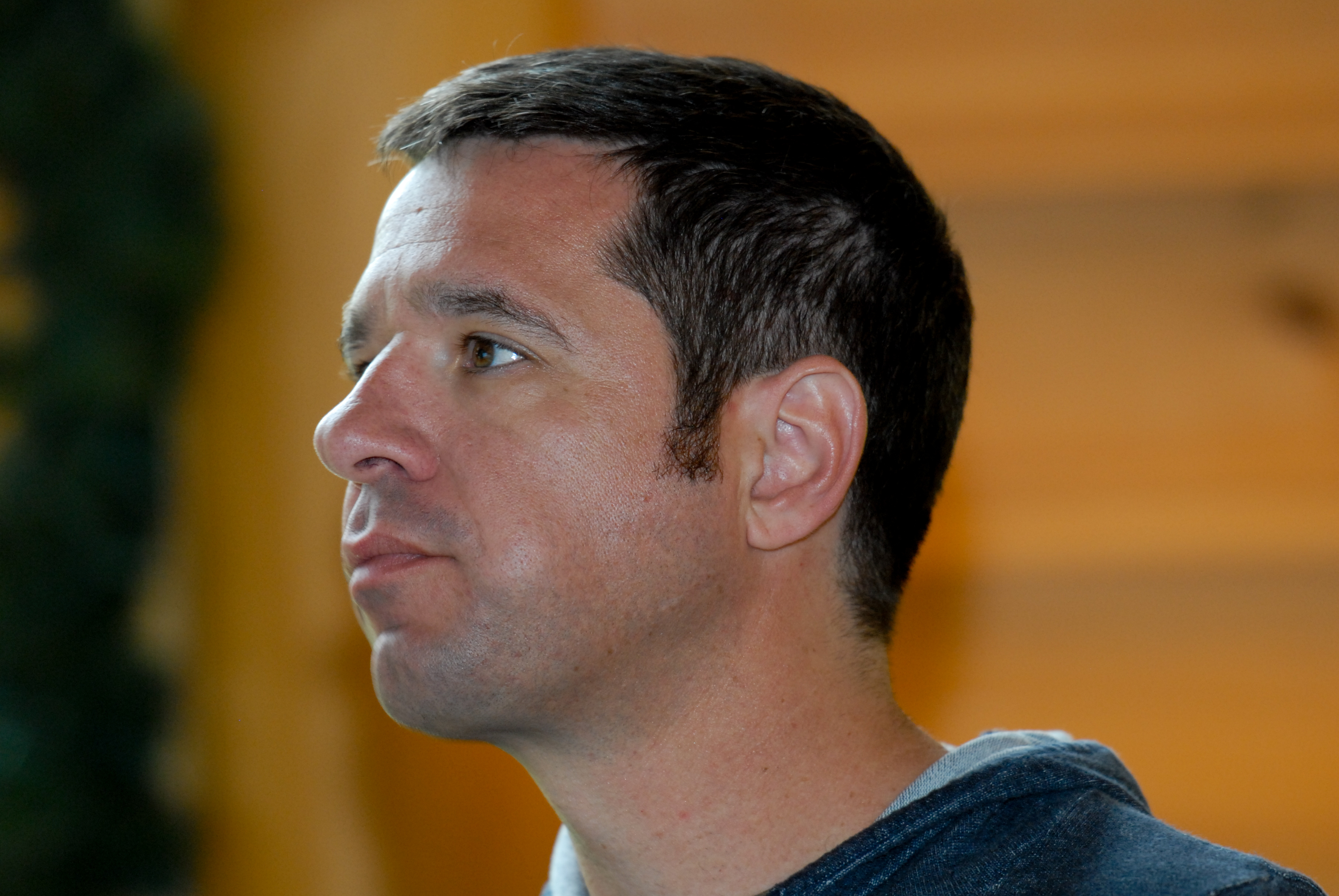 A person in a hoodie looks to the side with a focused expression in an indoor setting.