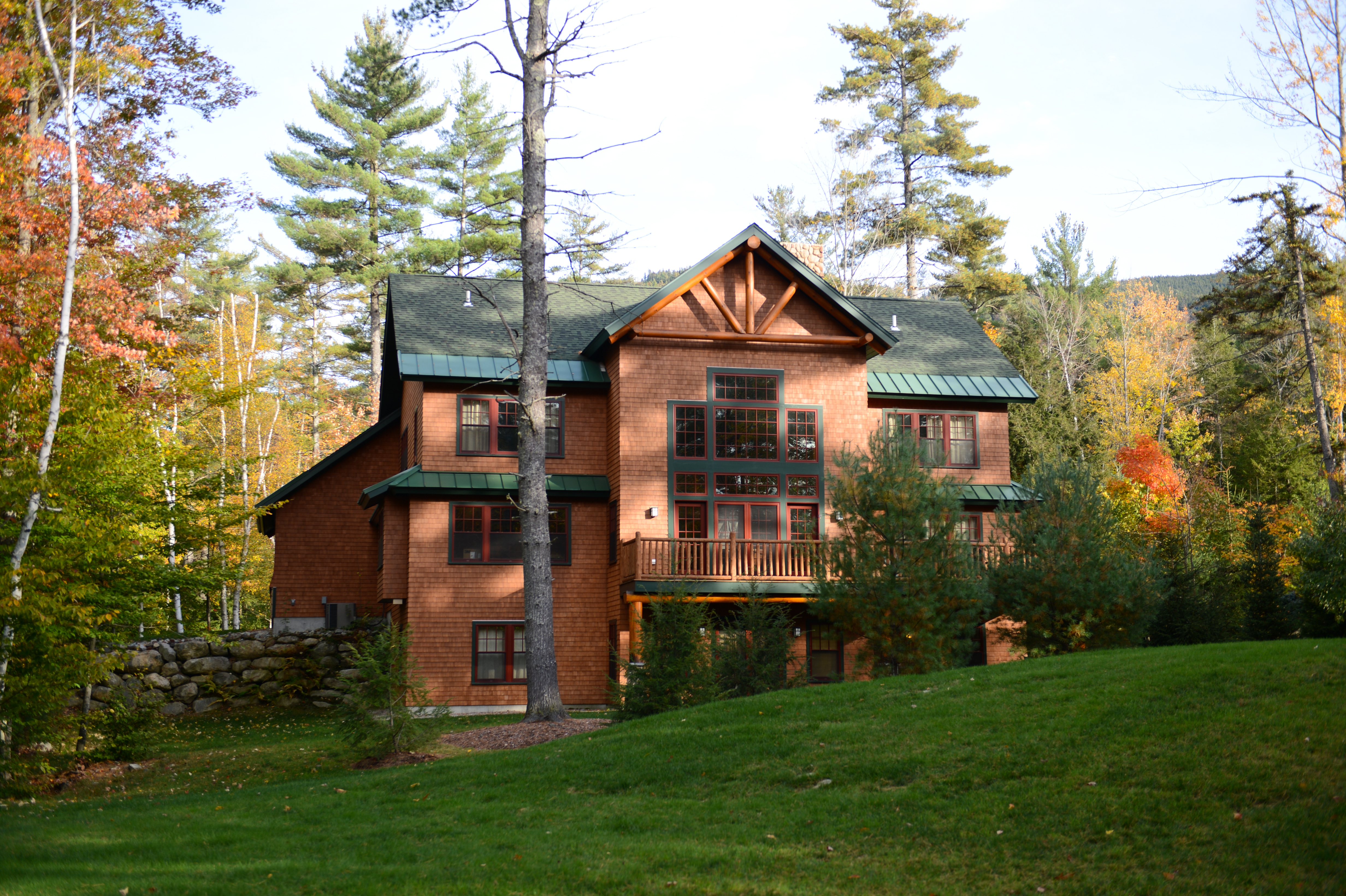 A large wooden house with green roofs surrounded by trees and grass, taken during daytime in autumn.