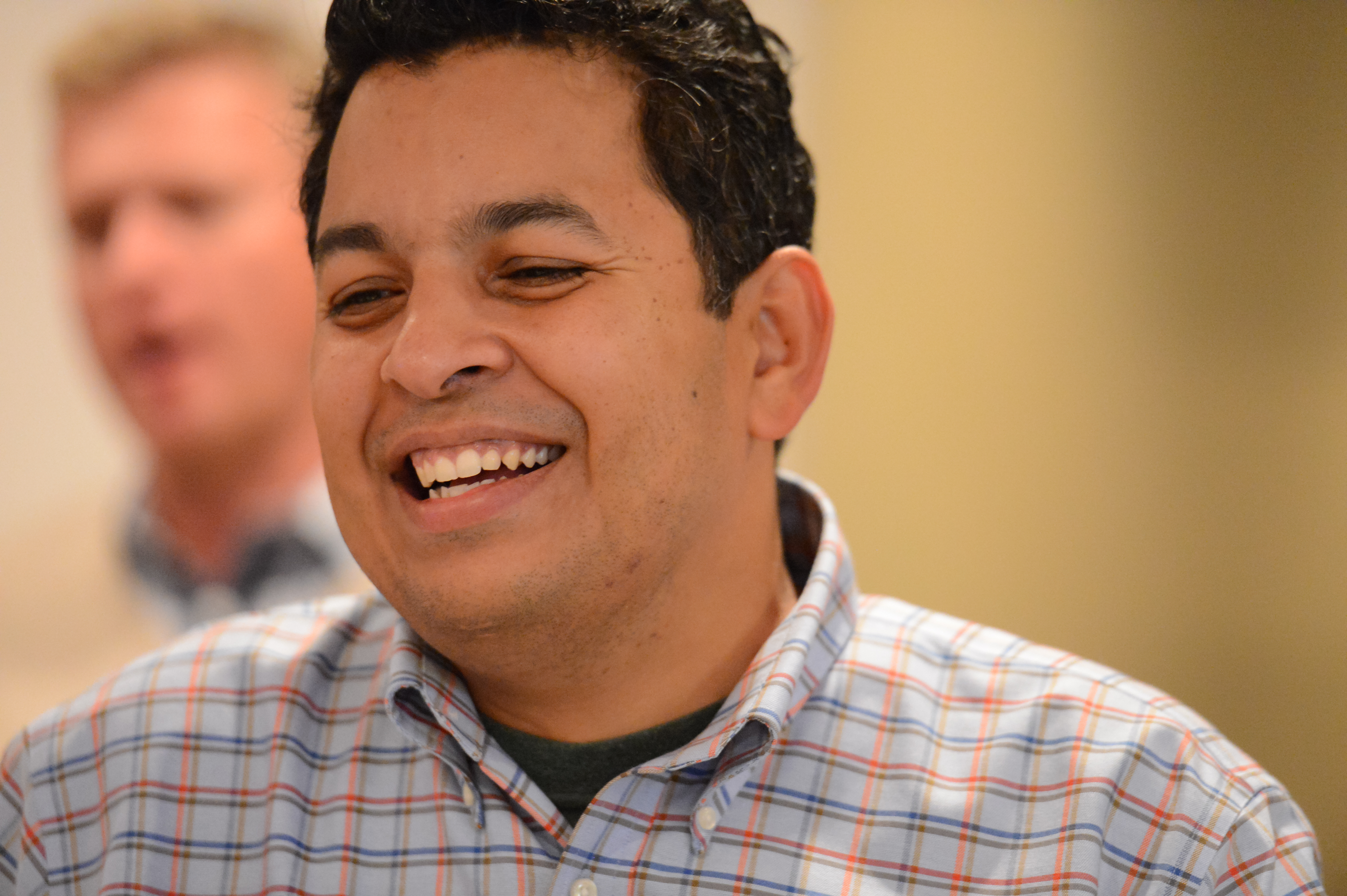 A man in a plaid shirt smiles while engaged in conversation at an Acquia offsite event.