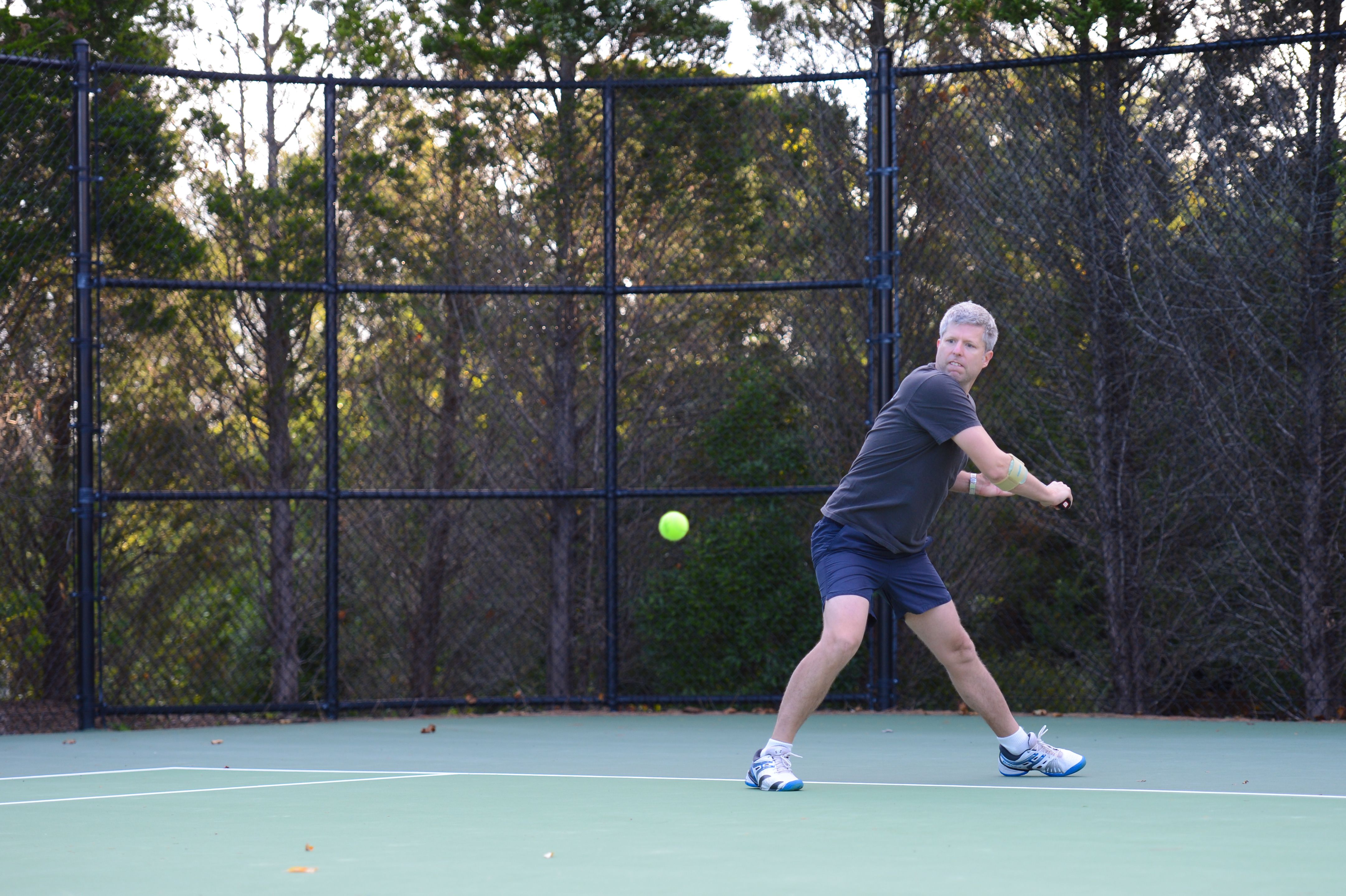 A man in sportswear prepares to hit a tennis ball with a backhand swing on an outdoor court.