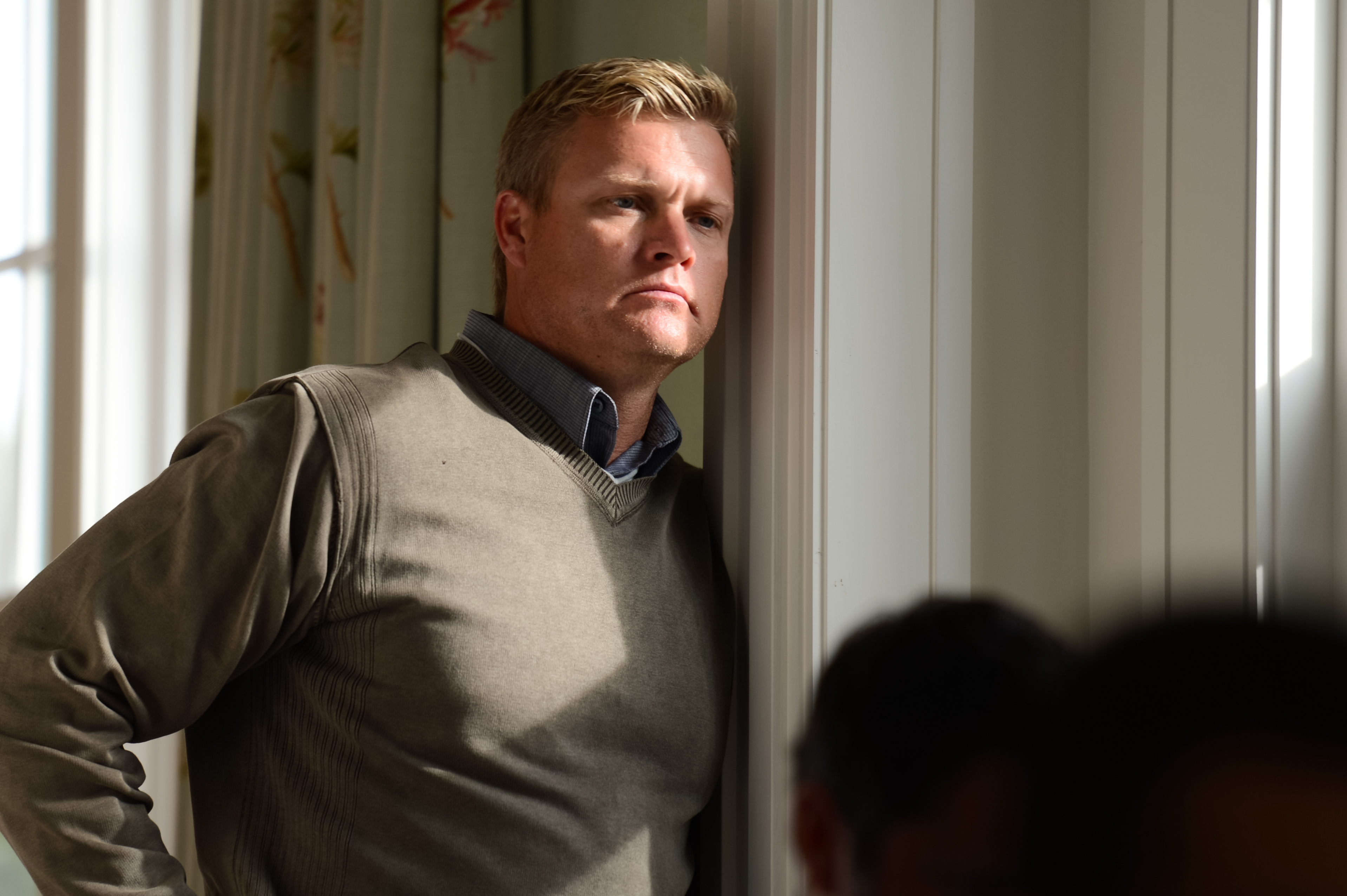 A man leans against a doorframe, looking thoughtful during an indoor event.