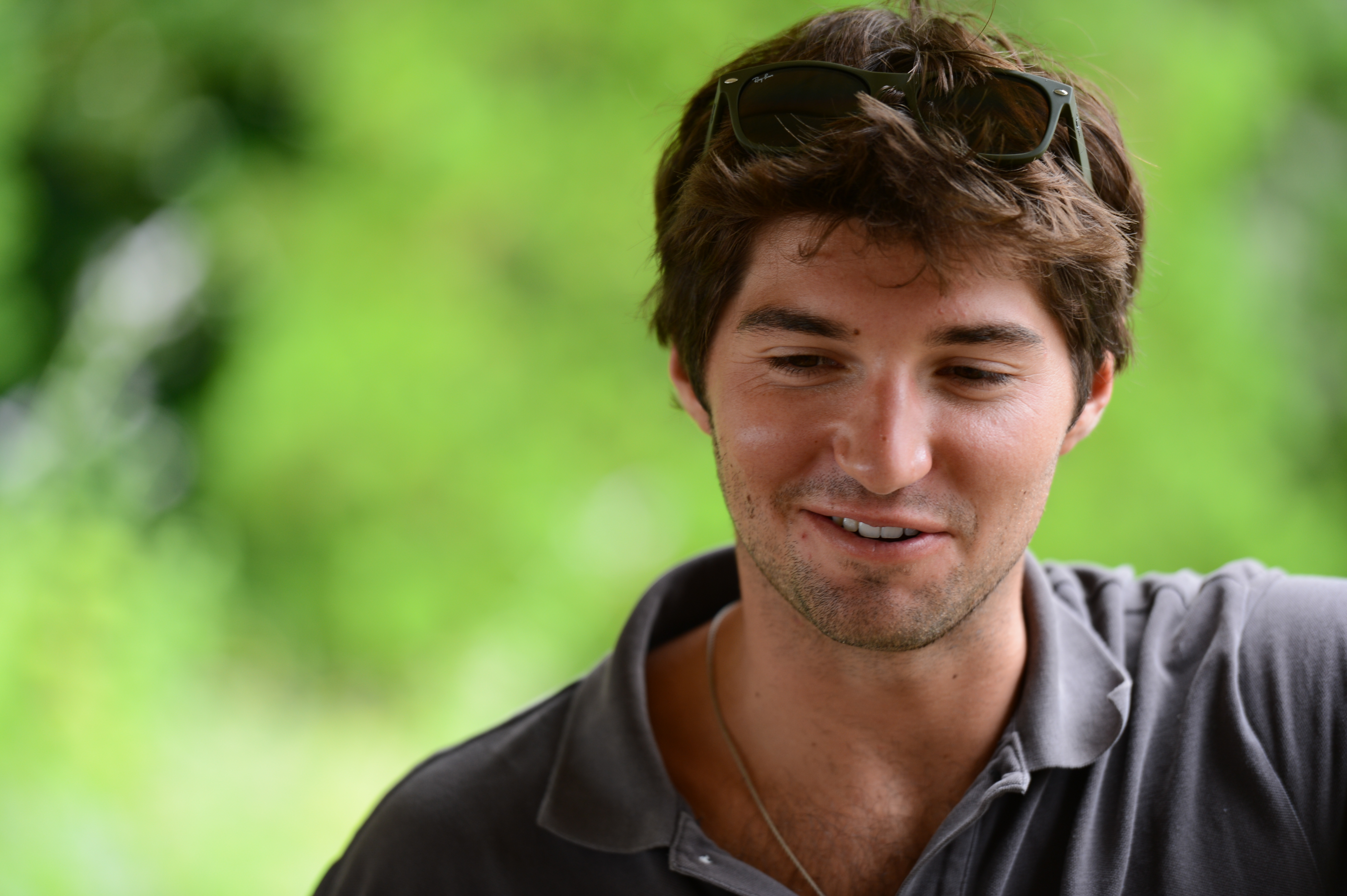 A man with sunglasses on his head smiles and looks down at something during an outdoor gathering.