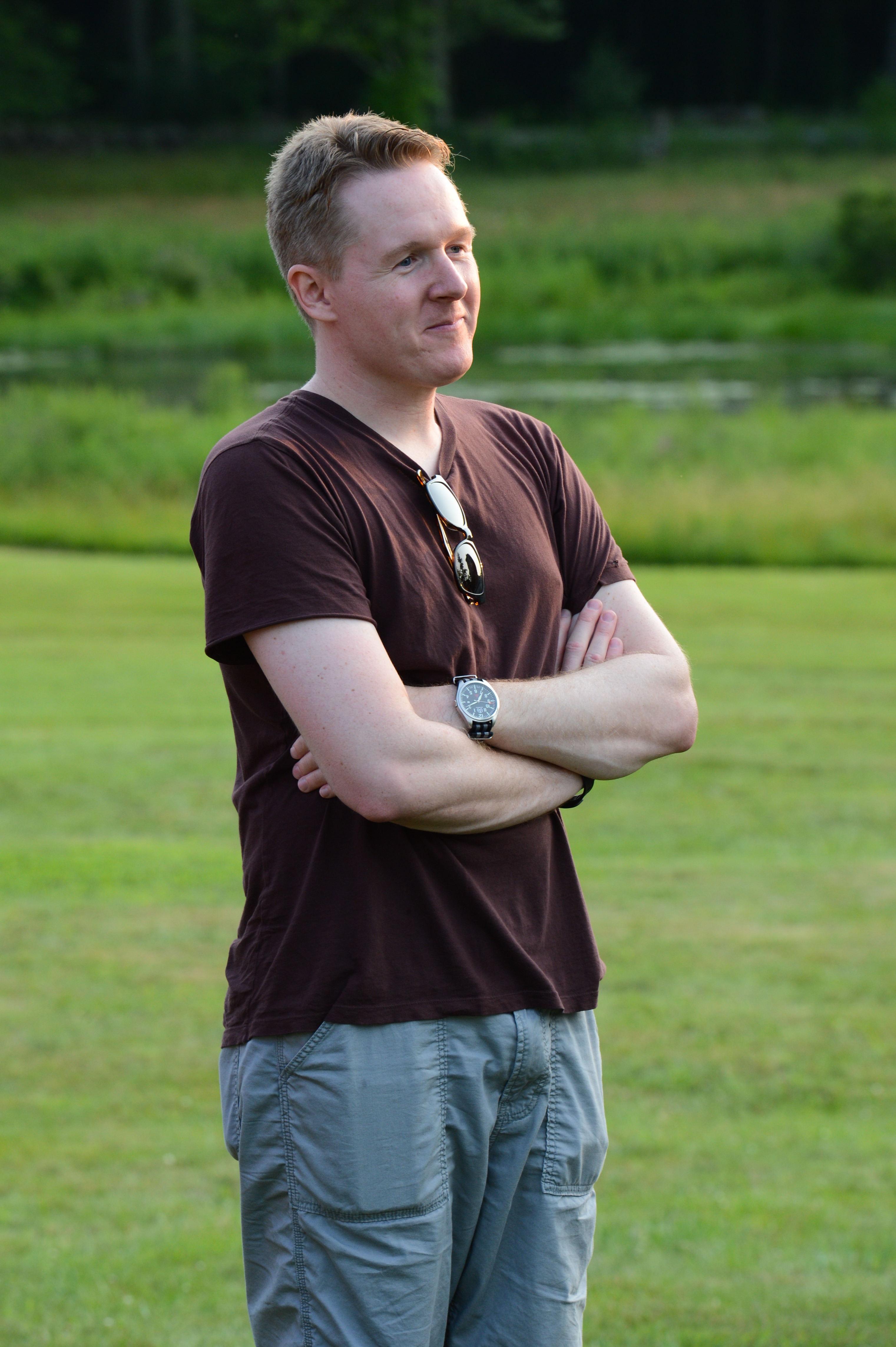A man stands on the grass with arms crossed, watching the dunk tank event at the summer party.