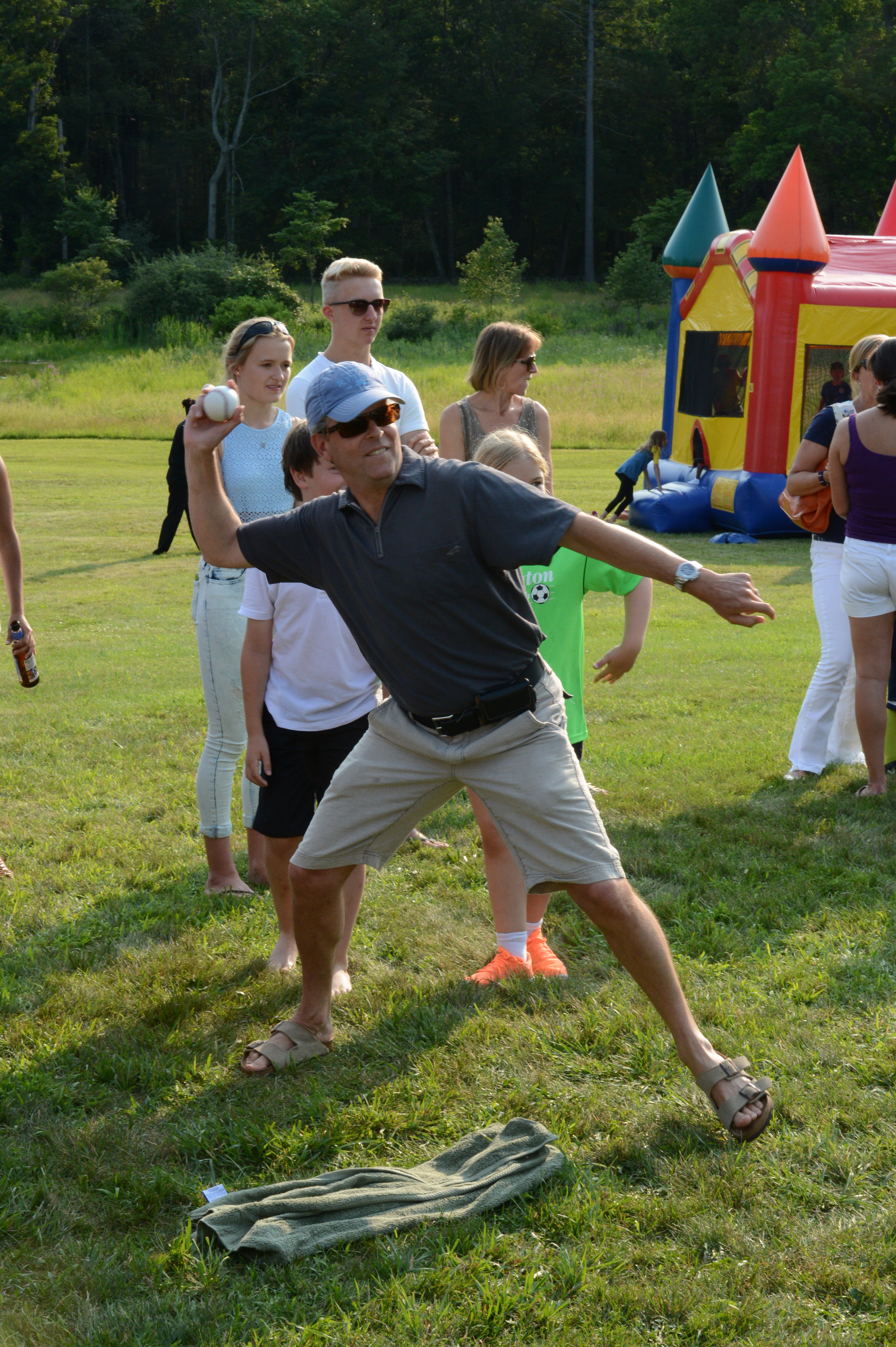 A man in sunglasses throws a ball toward a dunk tank target while others watch at an outdoor event.