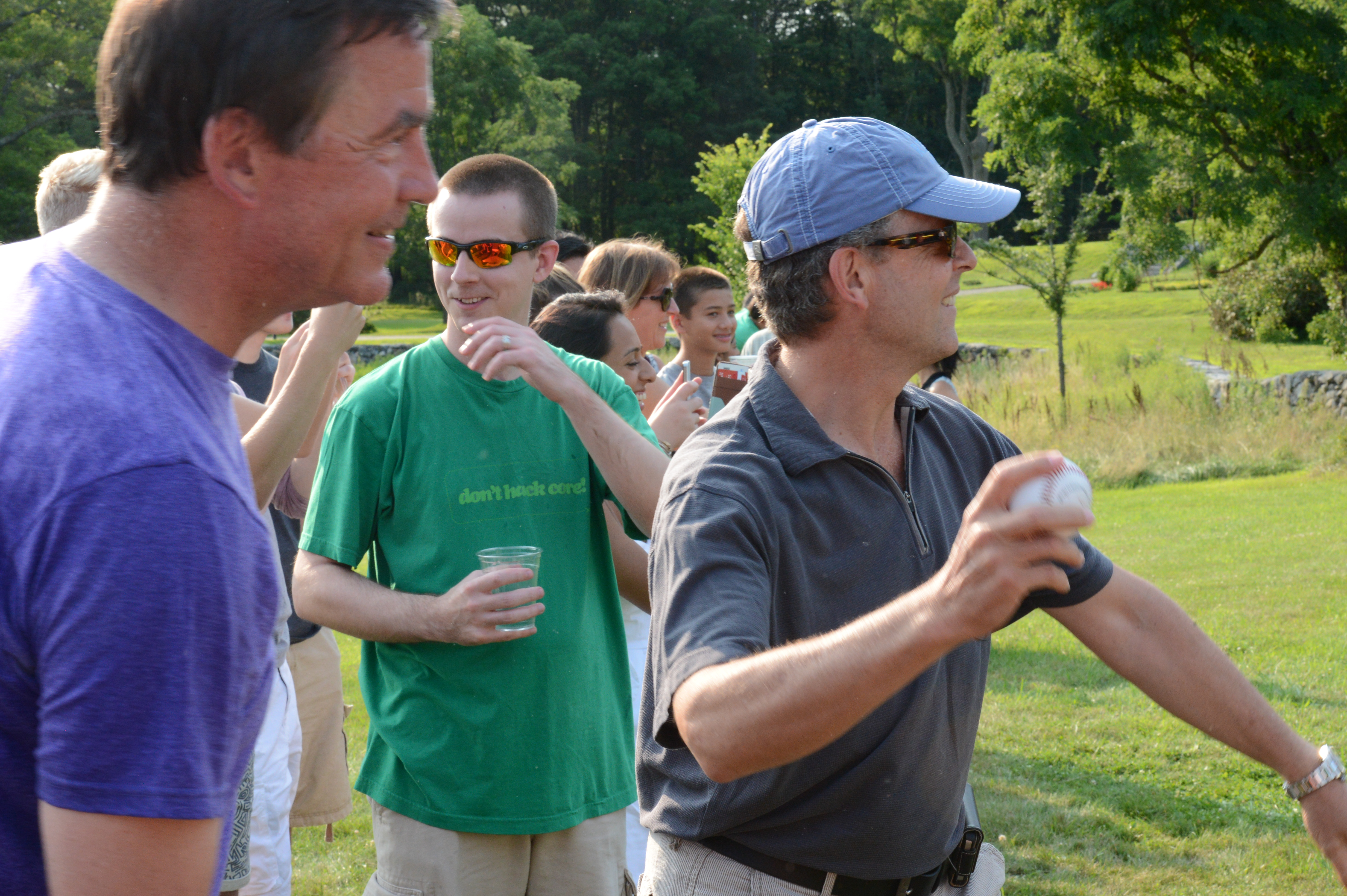 A man in a cap prepares to throw a ball at a dunk tank while others watch and cheer.