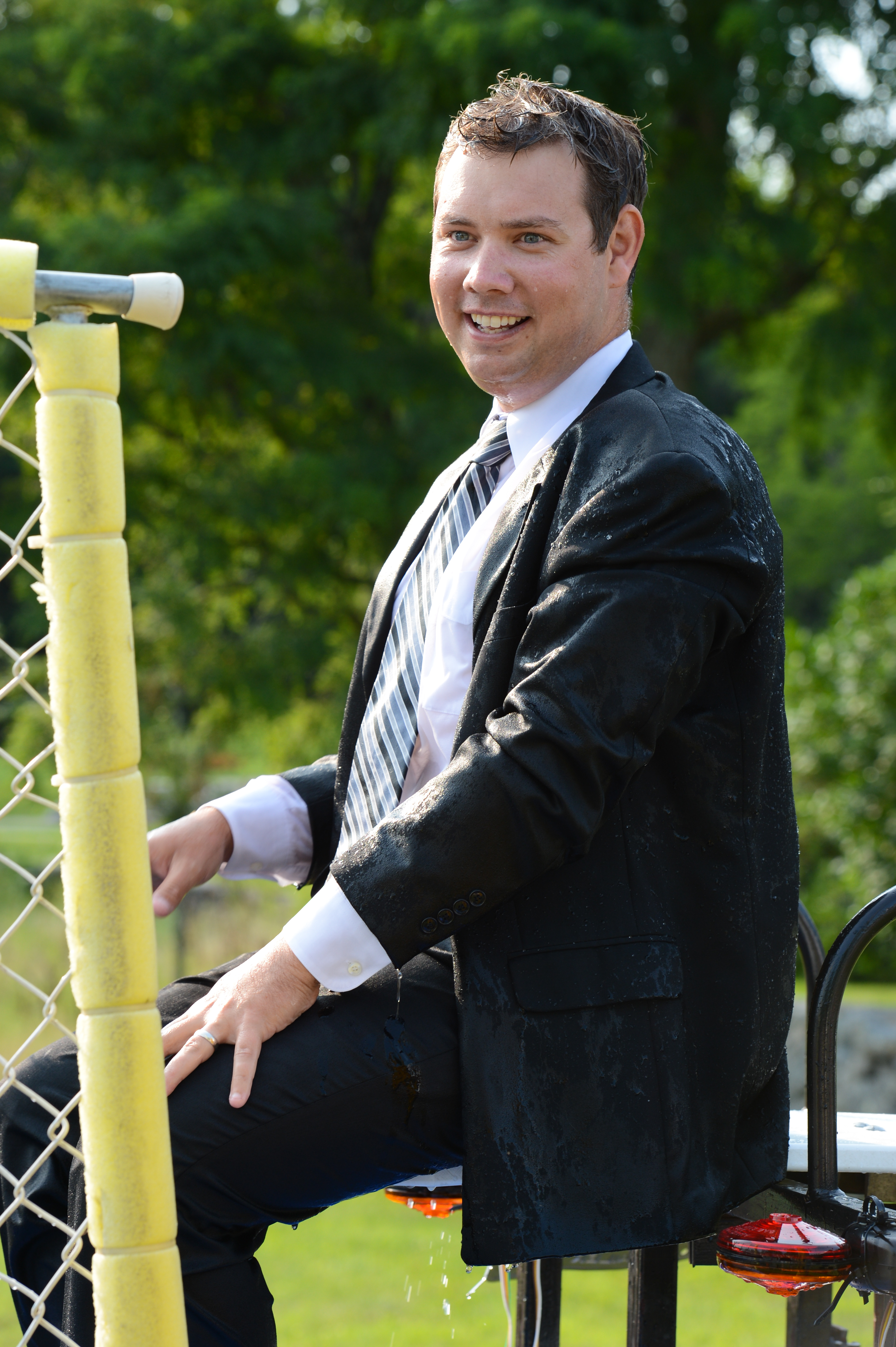 A man in a wet suit sits on a dunk tank platform, smiling after being dunked.