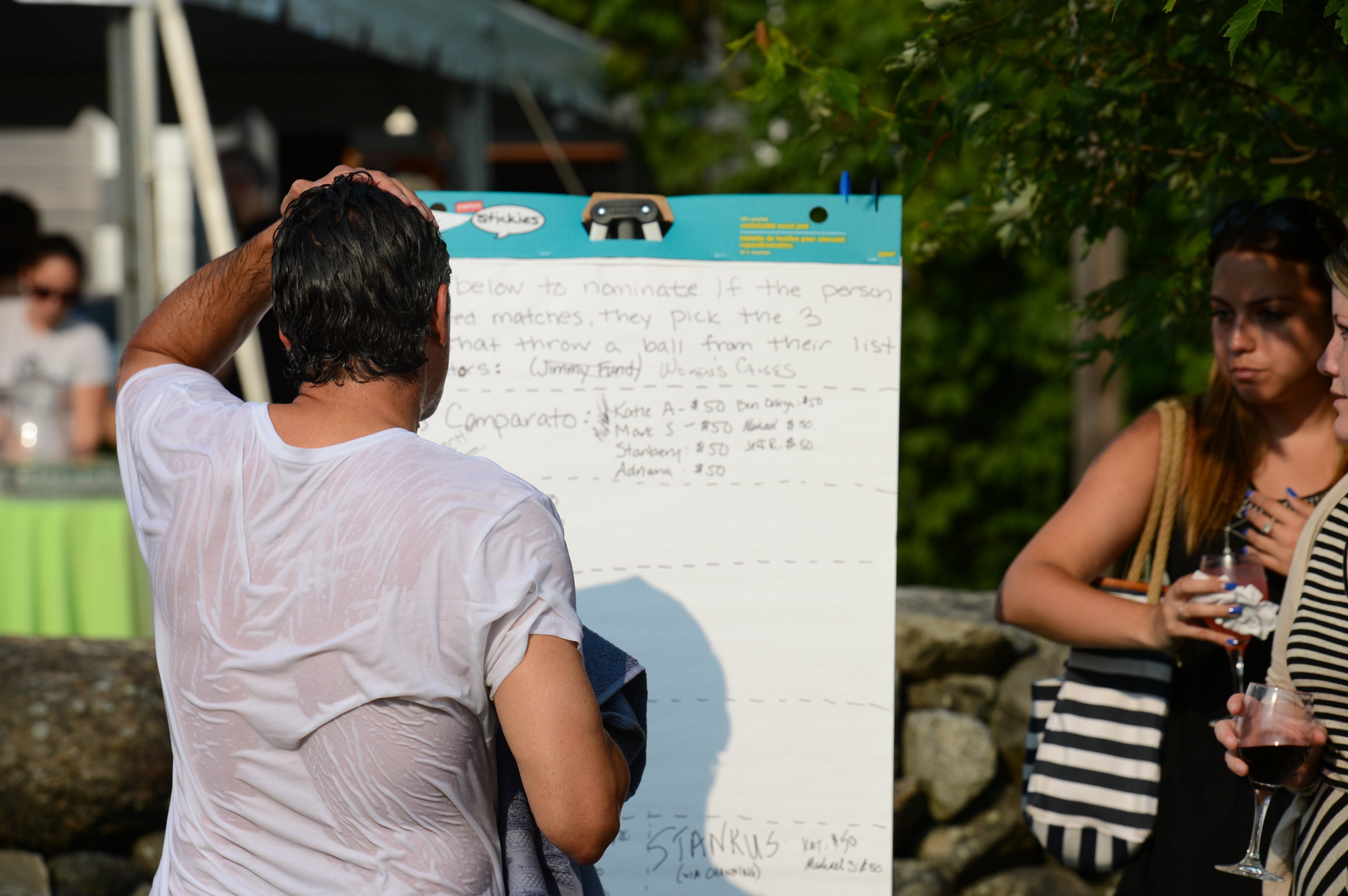 A soaked person wipes their head while standing near a sign at a dunk tank event.