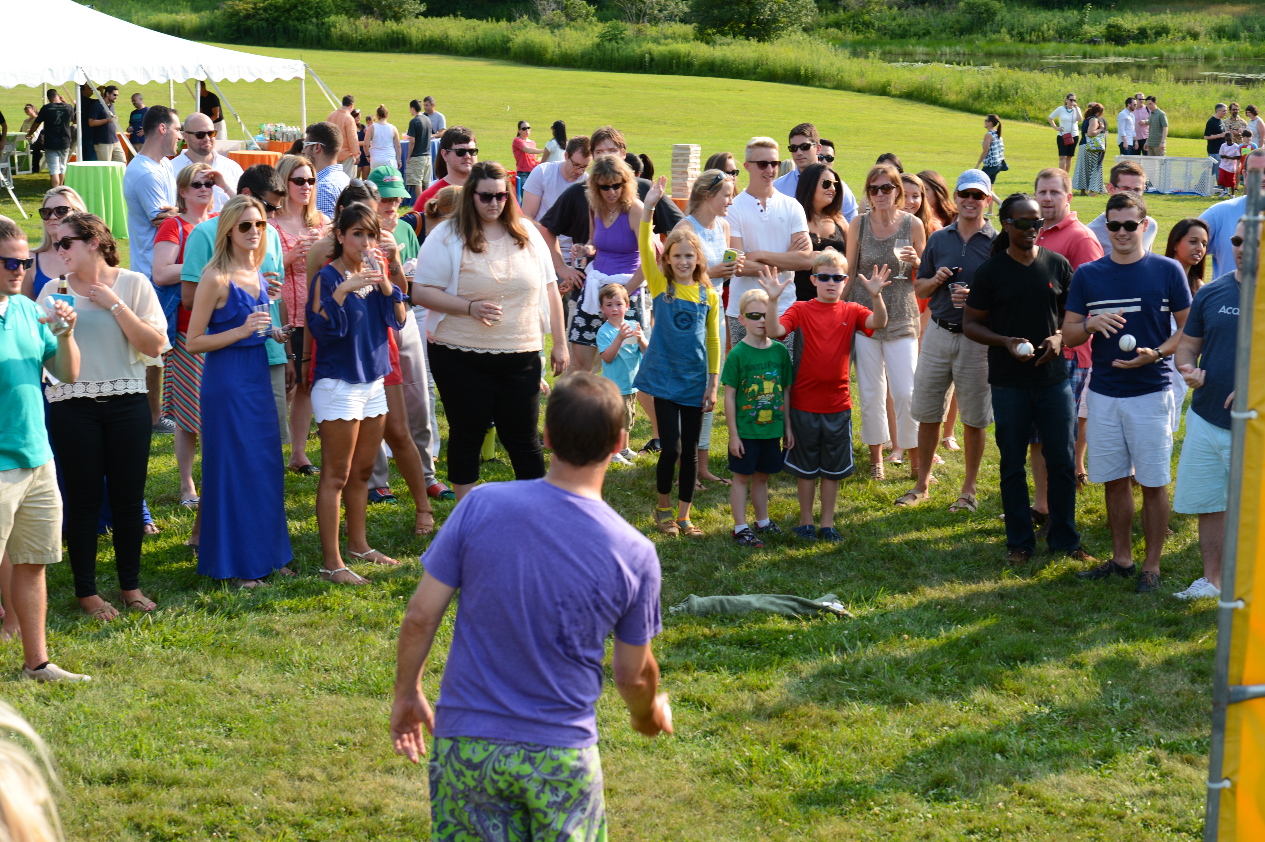 A crowd watches as a man in a purple shirt prepares to throw a ball at the dunk tank target.