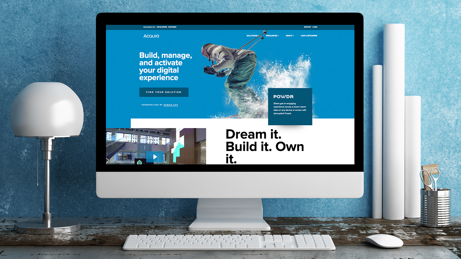 A computer screen shows the Acquia website with a slogan about building and managing digital experiences.