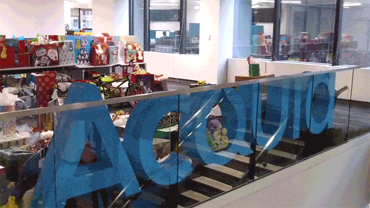 A collection of wrapped gifts and toys displayed in an office for the Acquia gift drive.
