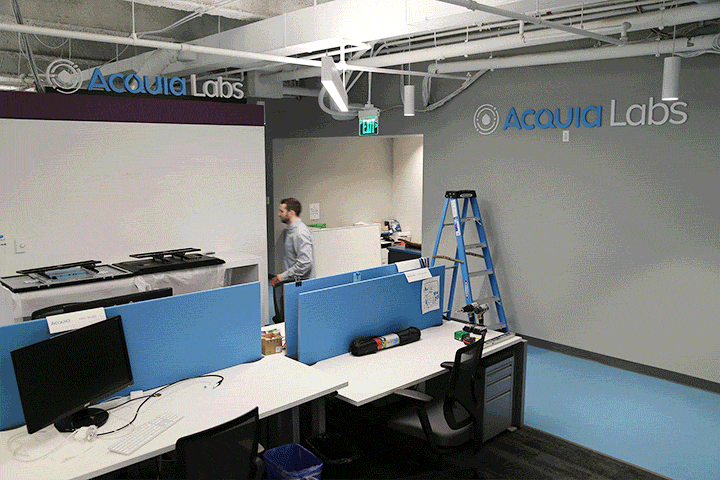 Workers install and adjust Acquia Labs signage on office walls in a timelapse sequence.