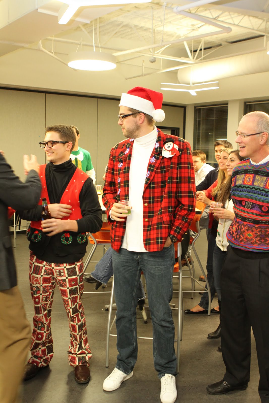 People in festive outfits chat and laugh at an office Christmas party.