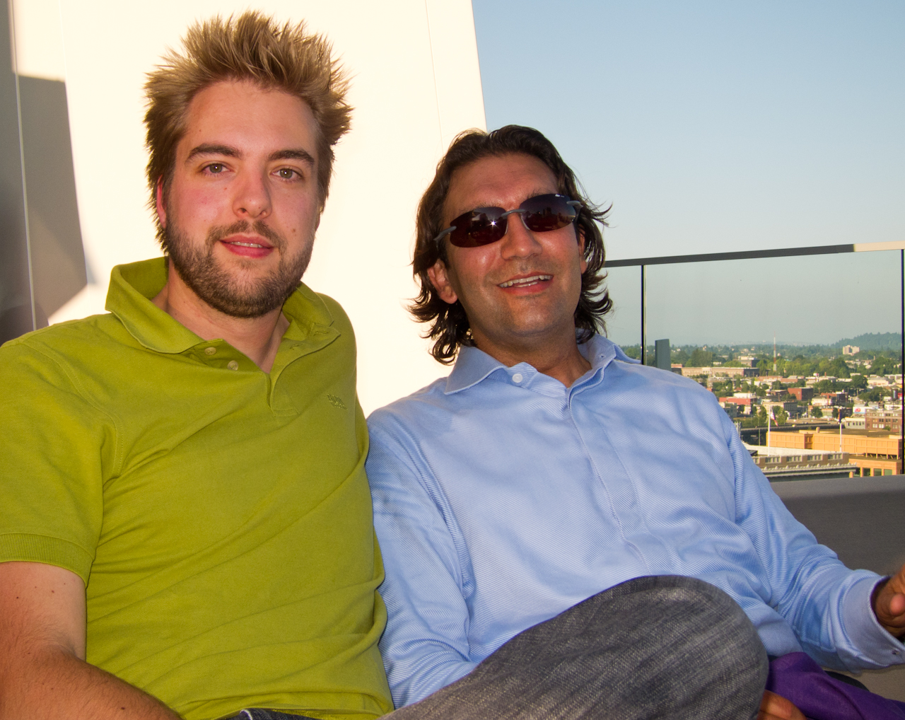 Two people sitting together on a rooftop, smiling at the camera.
