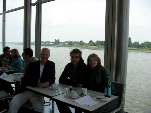 Three people sitting at a table with drinks, smiling at the camera in a restaurant.