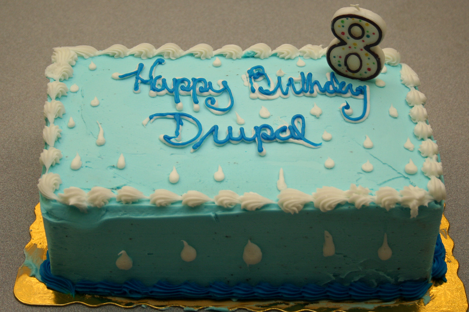 A blue birthday cake with "Happy Birthday Drupal" written in icing and a number 8 candle on top.