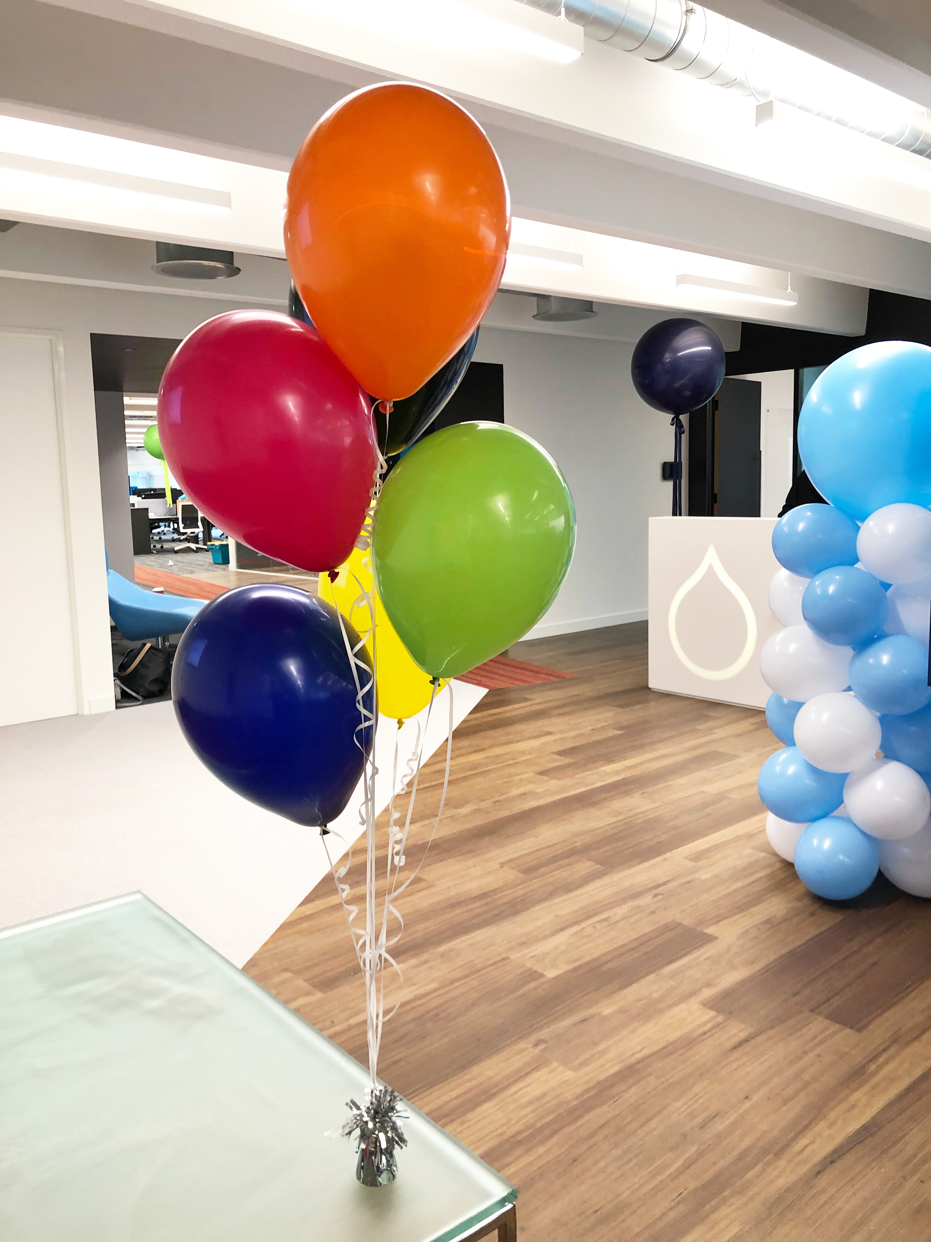 Colorful balloons tied to a small weight on a glass table in an office space.