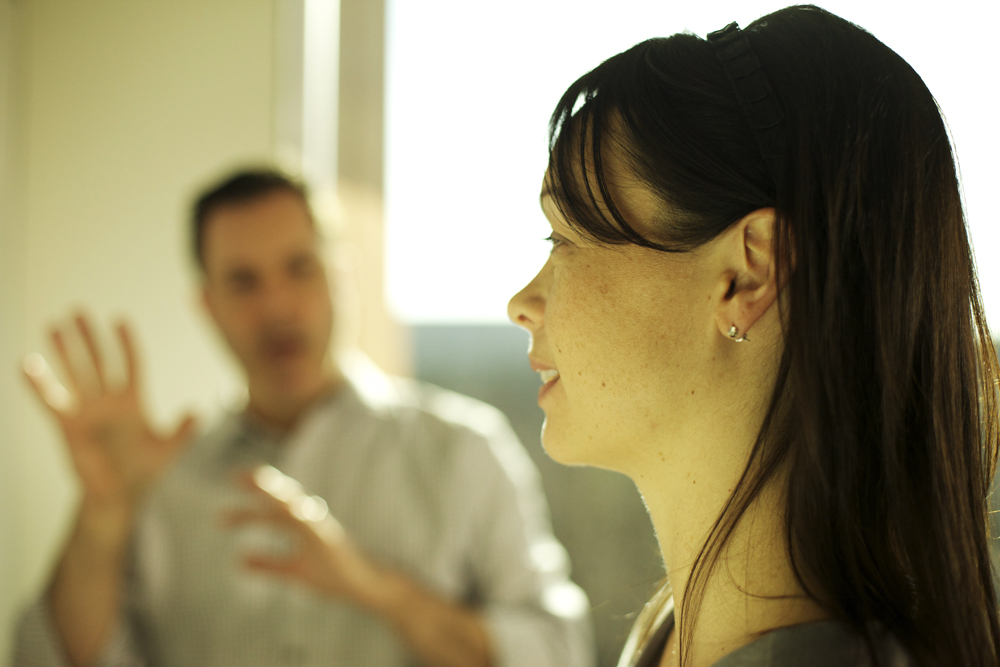 A woman listens attentively while a man in the background gestures as he speaks.