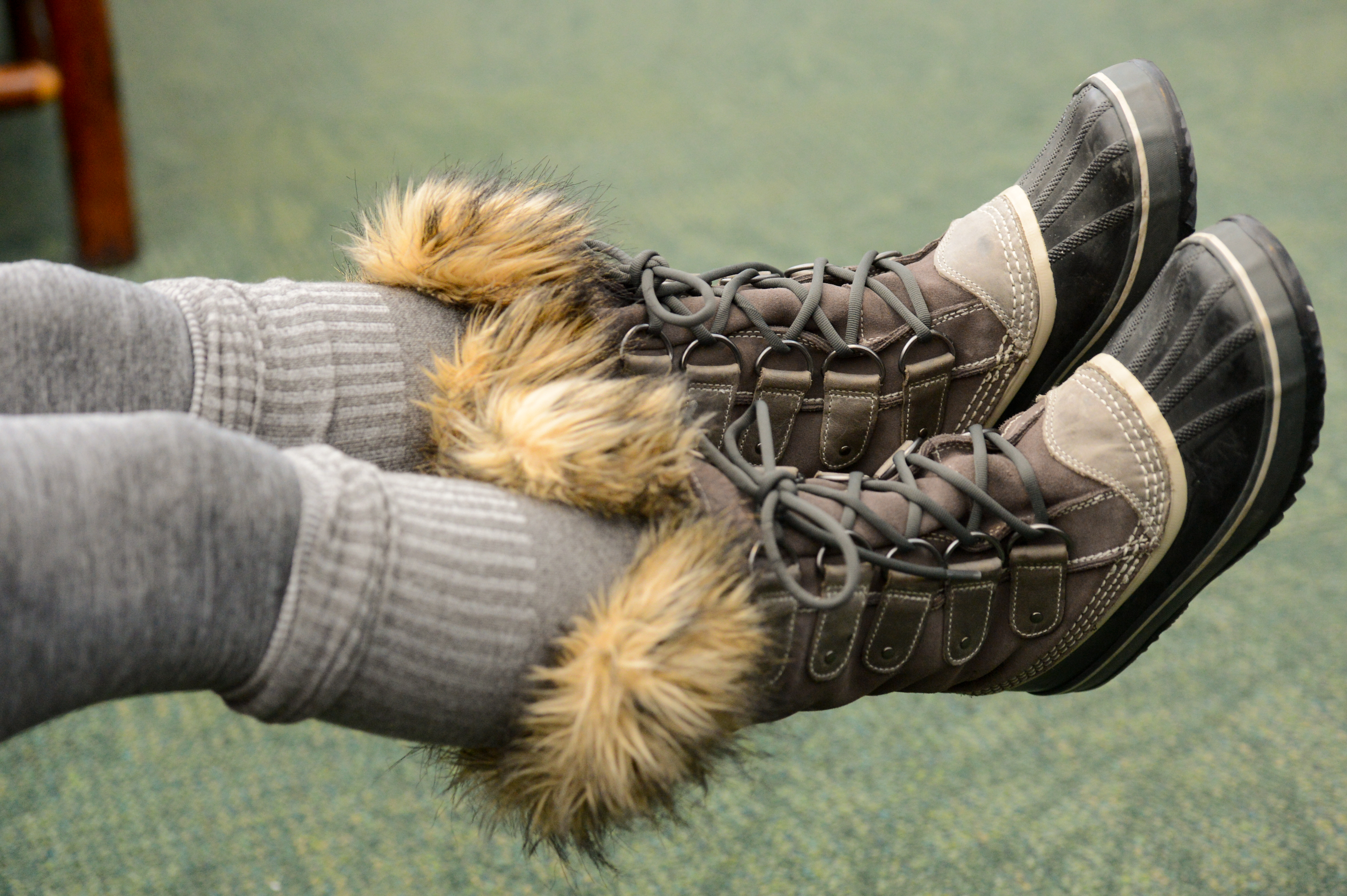 A person wearing gray leggings and fur-lined winter boots rests their feet in the air.