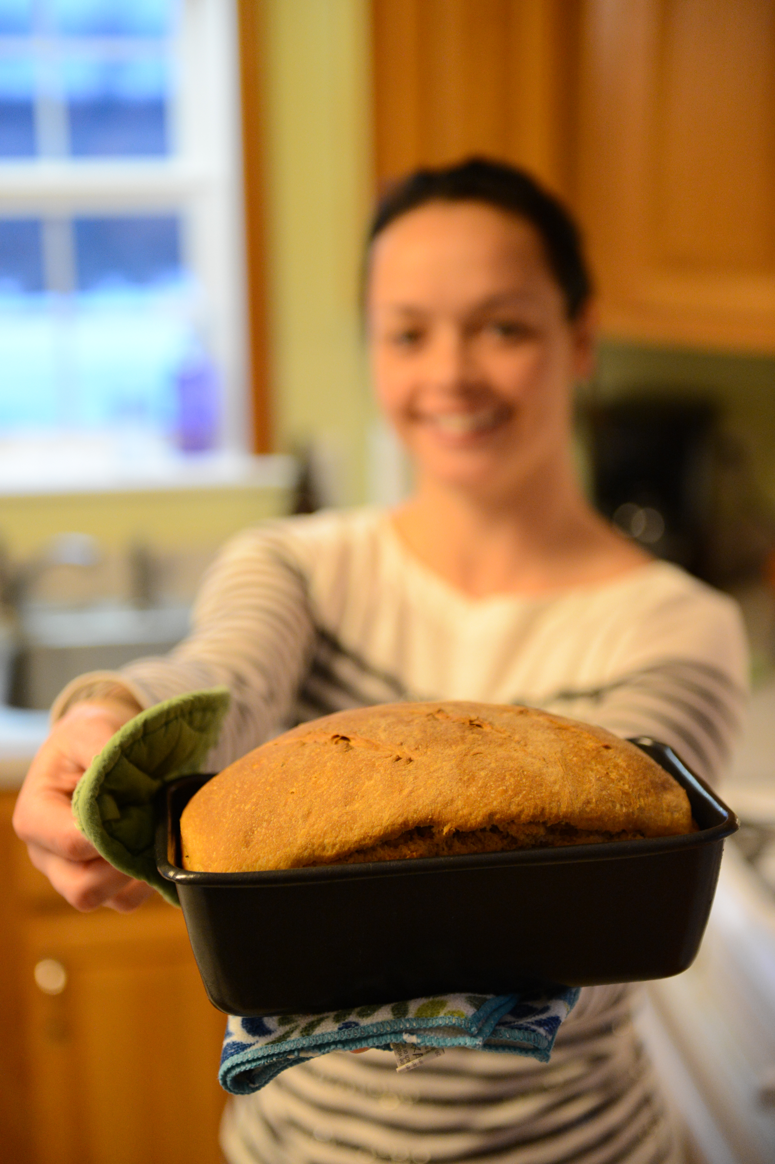 A person holds out a freshly baked loaf of bread in a black pan, using an oven mitt.