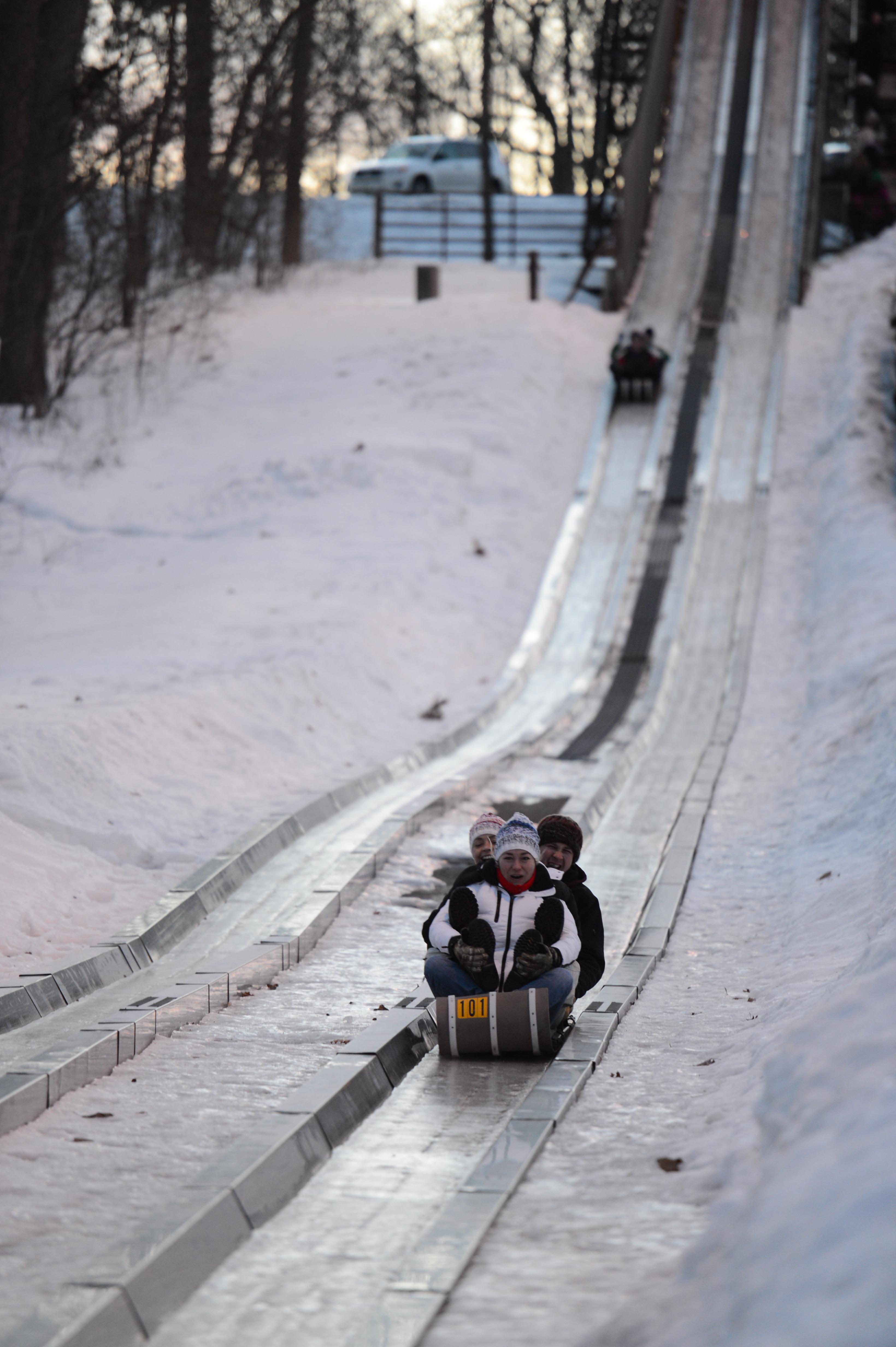 Three people ride a toboggan down an icy track, dressed in winter clothing and hats.