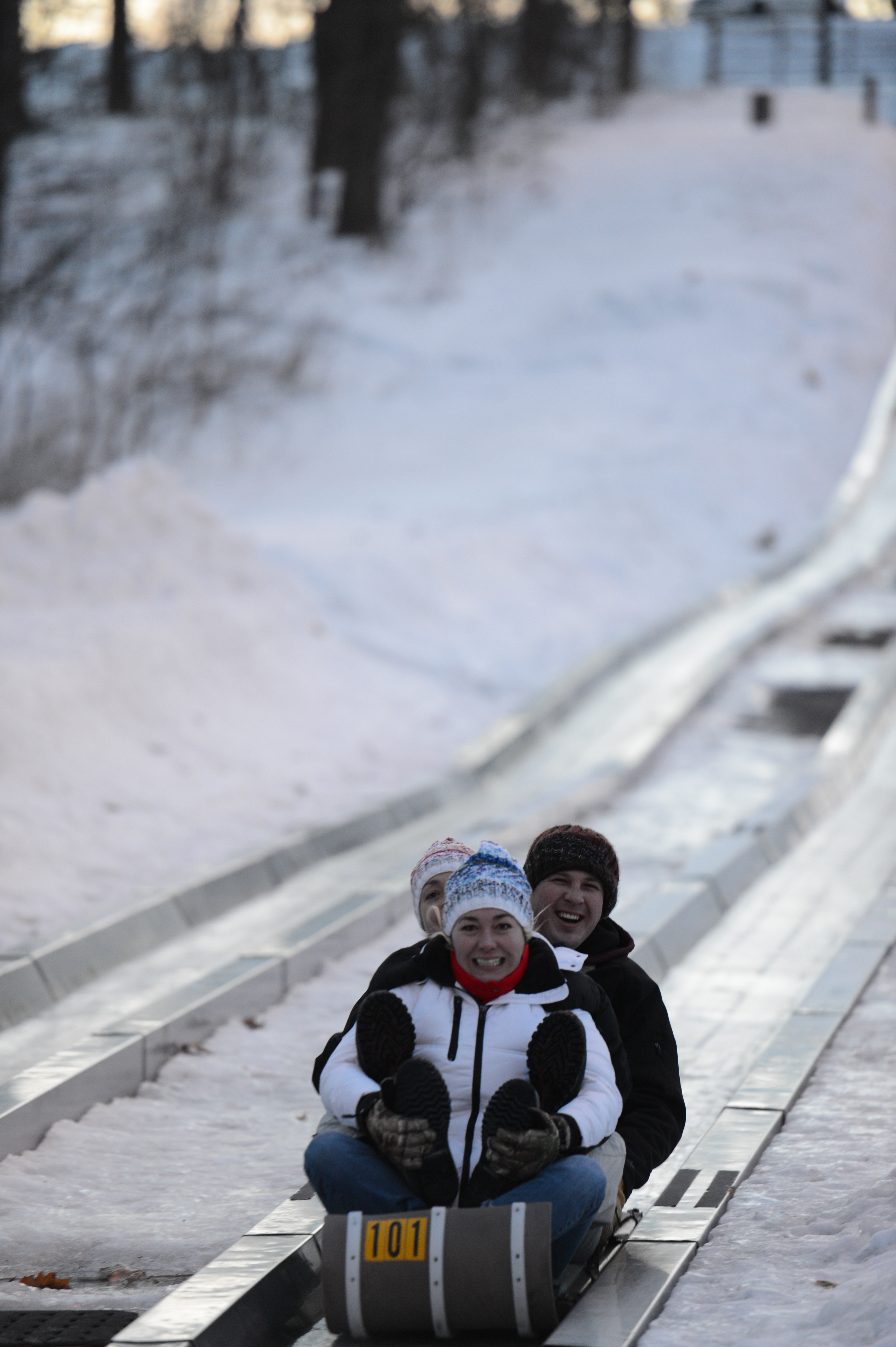 Three people in winter clothing ride a sled down an icy track, smiling and enjoying the snowy outdoor activity.