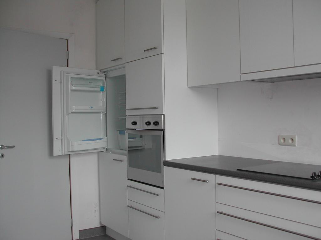 Empty kitchen with white cabinets, a black countertop, and an open refrigerator, photographed before moving in March 2003.
