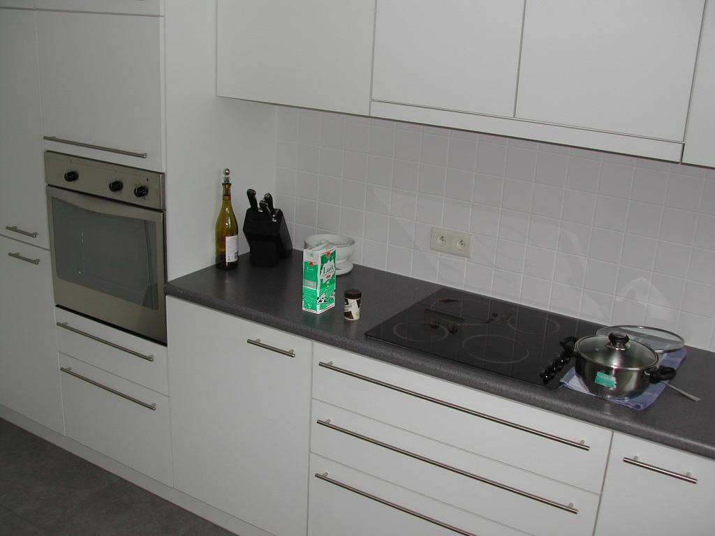 A modern kitchen with white cabinets, an oven, a stovetop, and various items on the countertop, including cookware.